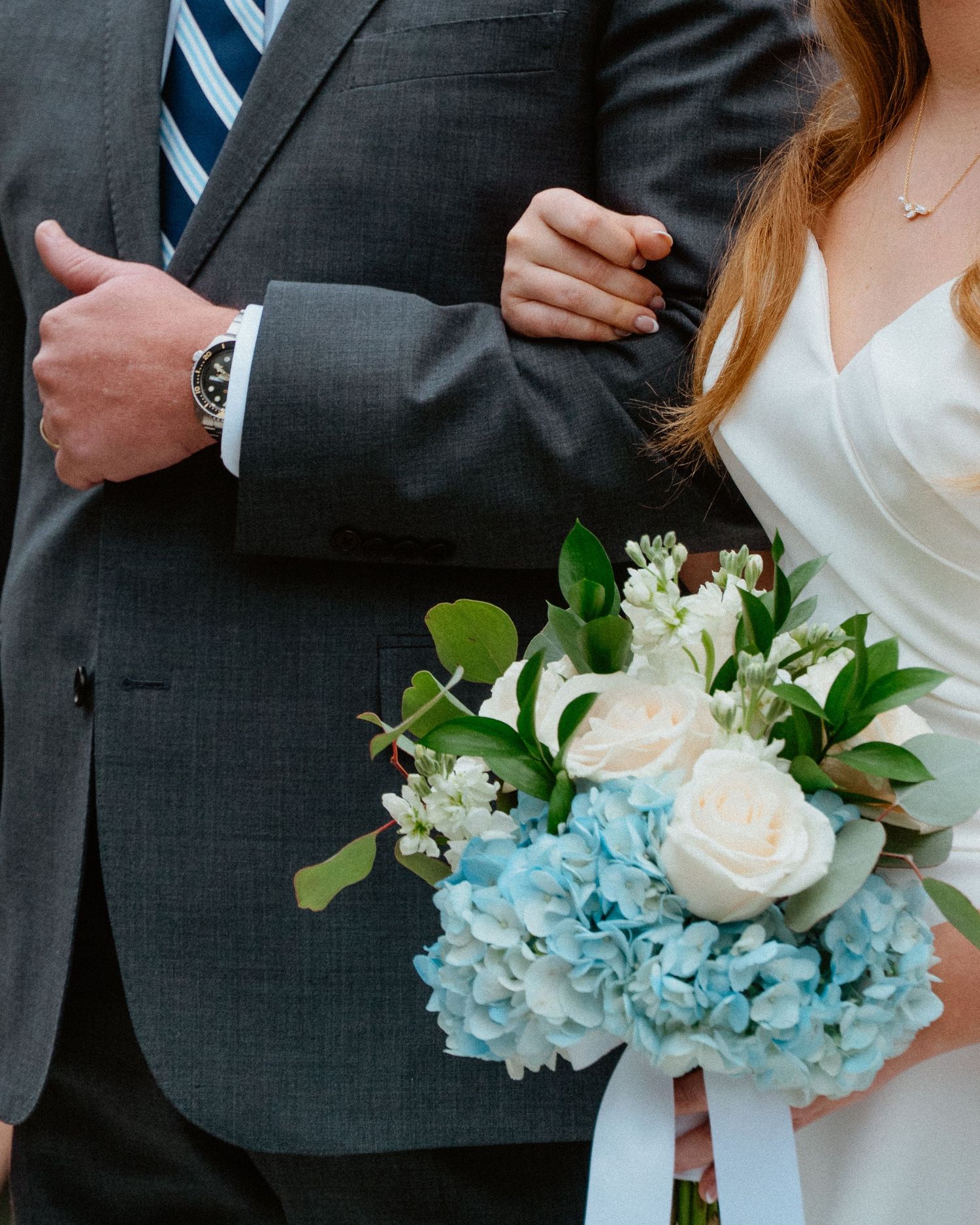 Bride holding a blue hydrangea and white rose bouquet while standing beside a groomsman.