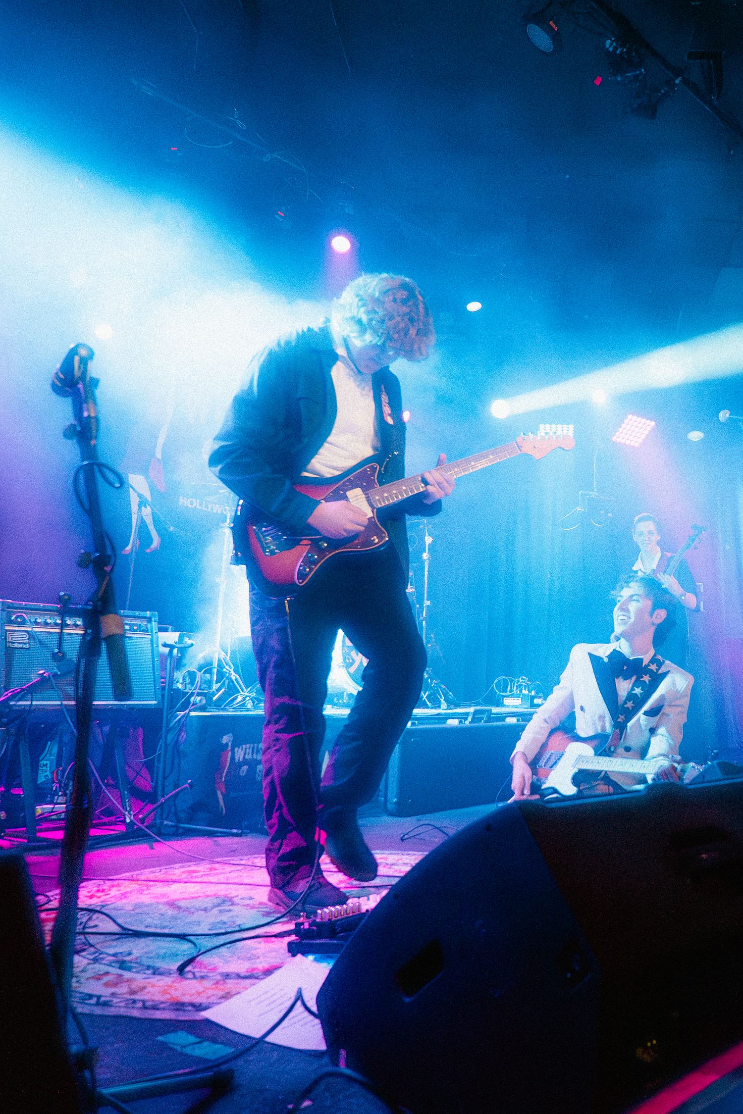 A musician plays an electric guitar against a blue and purple background.