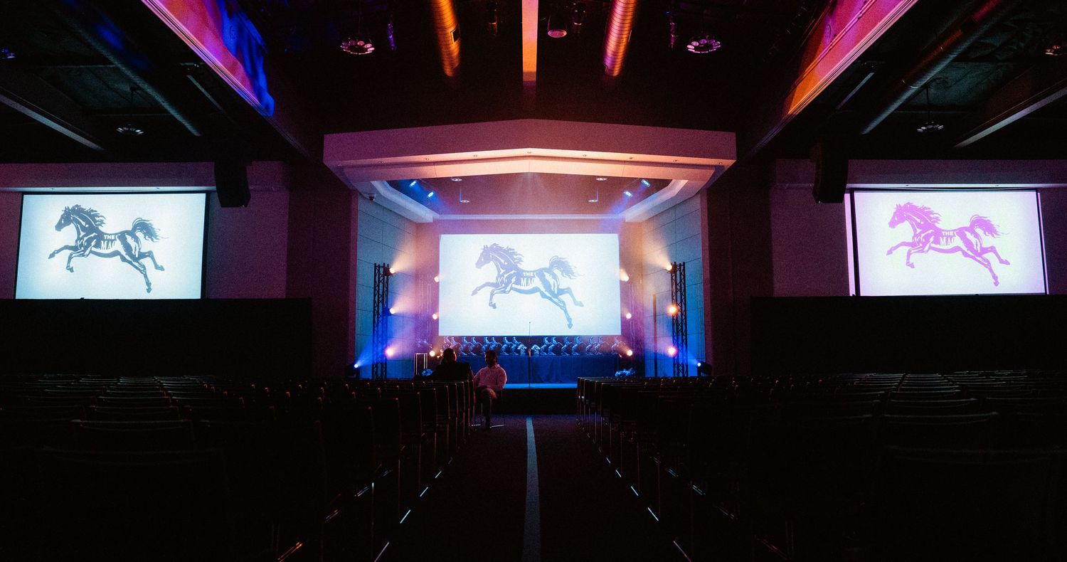 Elegant event venue with horse logo projected on three screens, colorful stage lighting in blue and red tones.