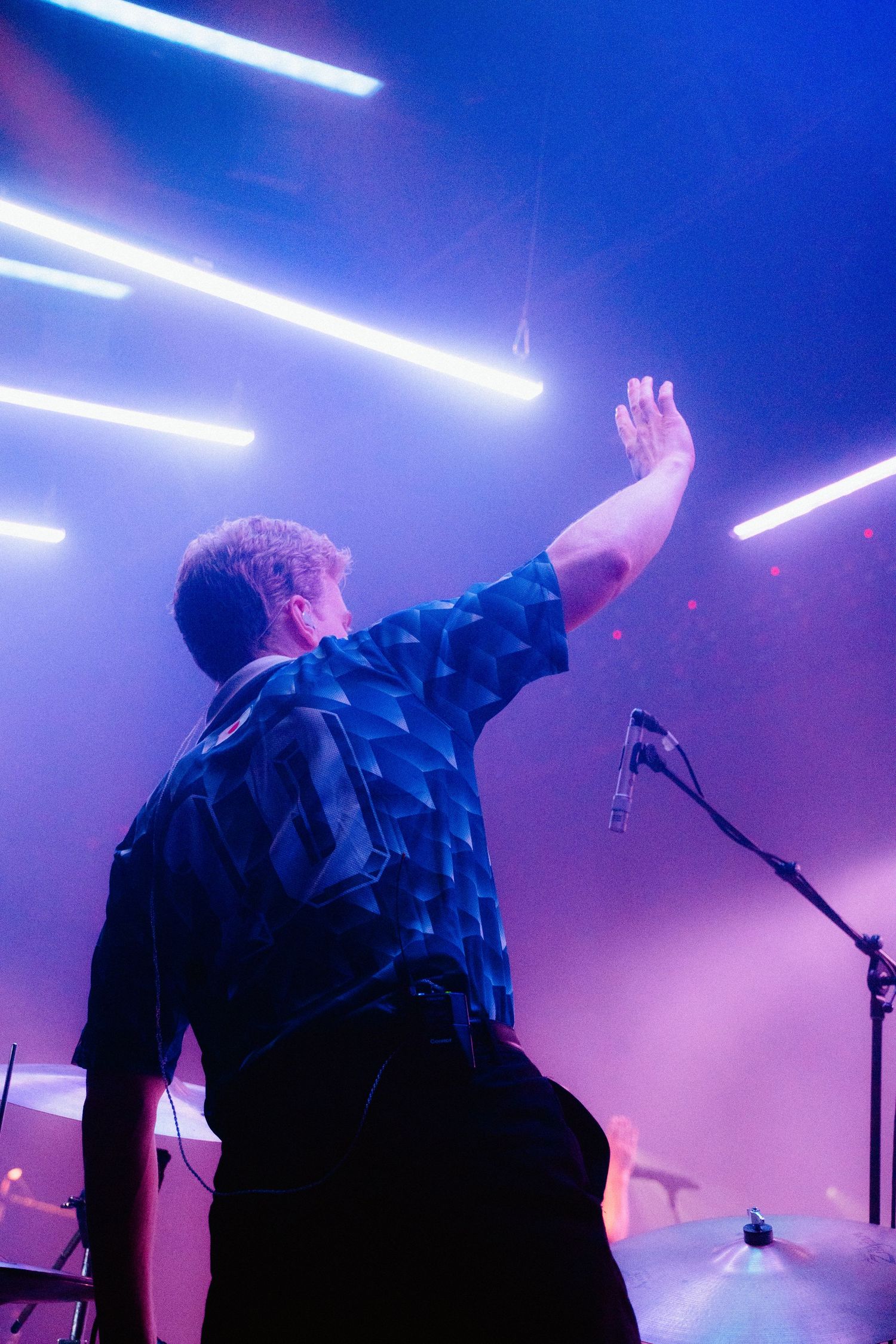 A musician wearing a sports jersey waves at the crowd as bright lights shine above him.