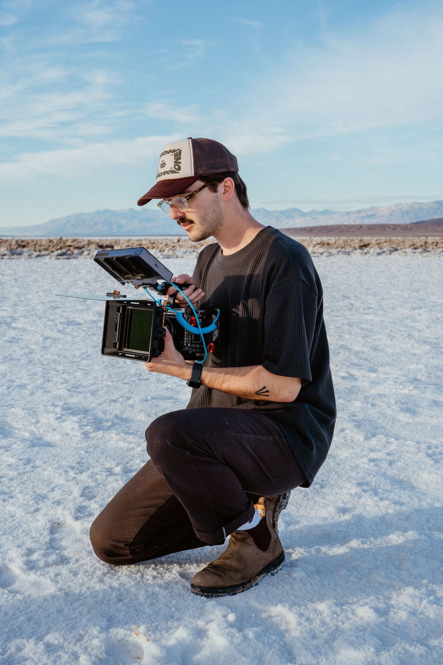 A cinematographer crouches on a salt flat while reviewing footage on a professional cinema camera rig.
