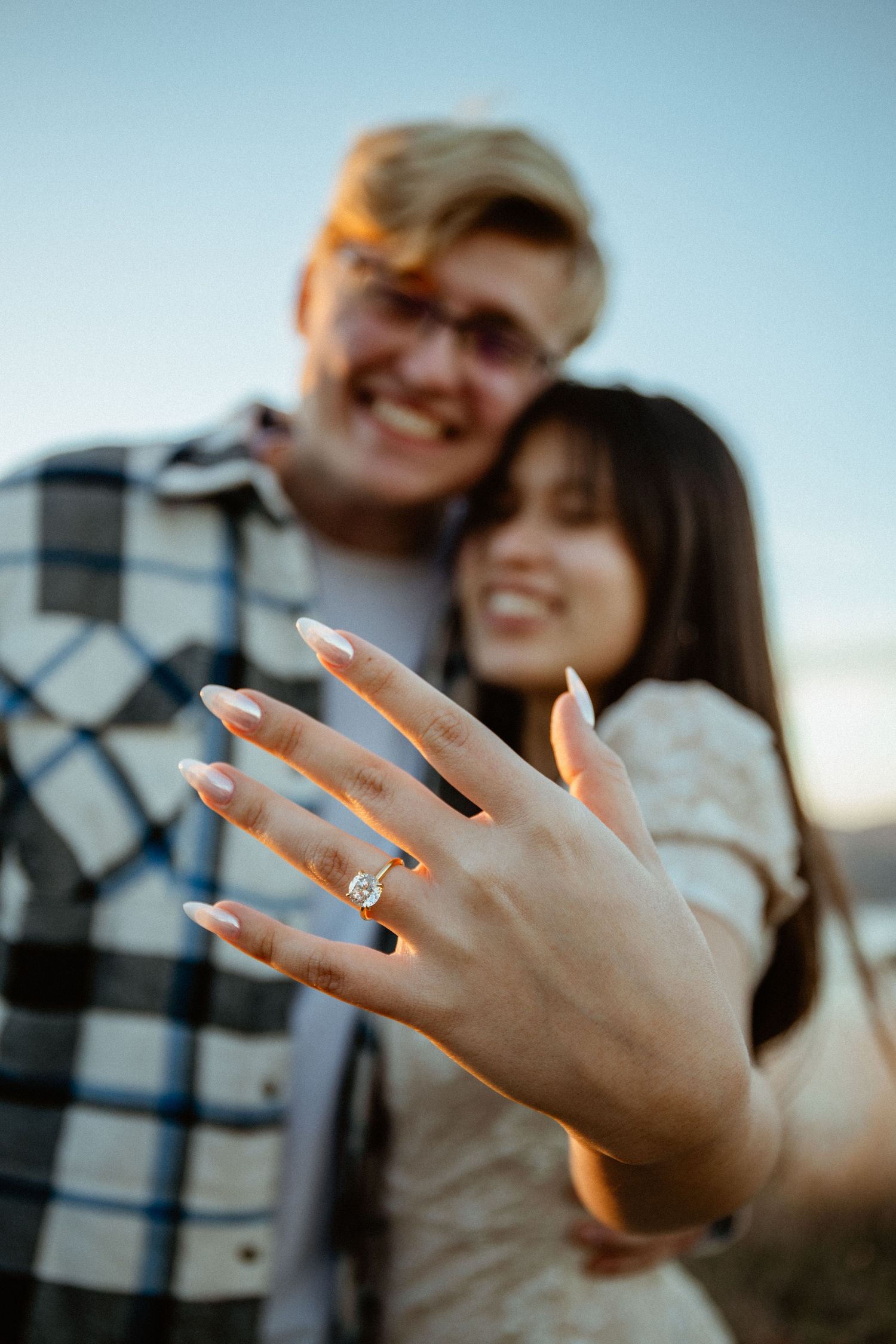 Smiling couple showing off oval diamond engagement ring after outdoor mountain proposal.
