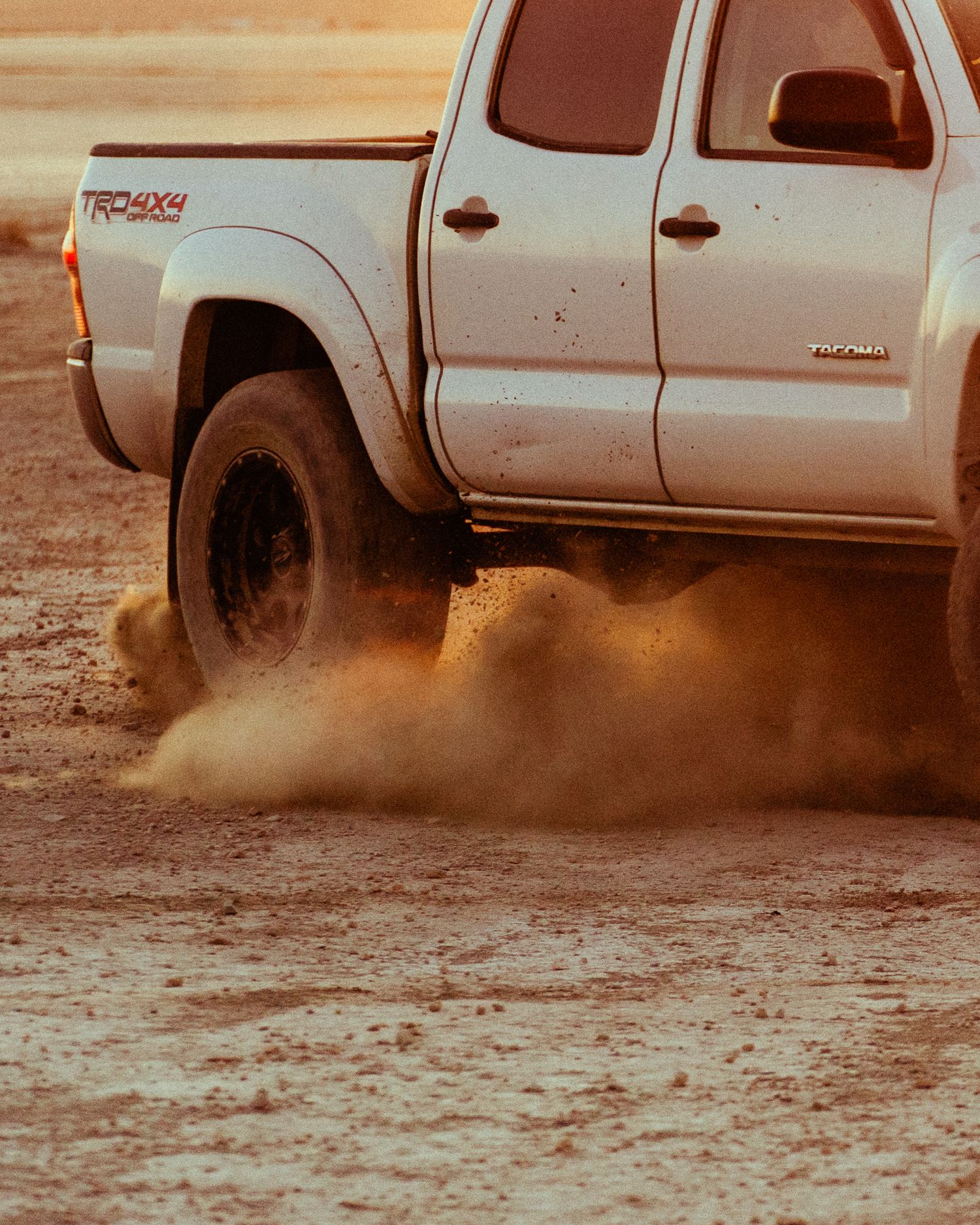 Close-up of Toyota Tacoma TRD 4x4 rear wheel spinning in dirt kicking up dust cloud.