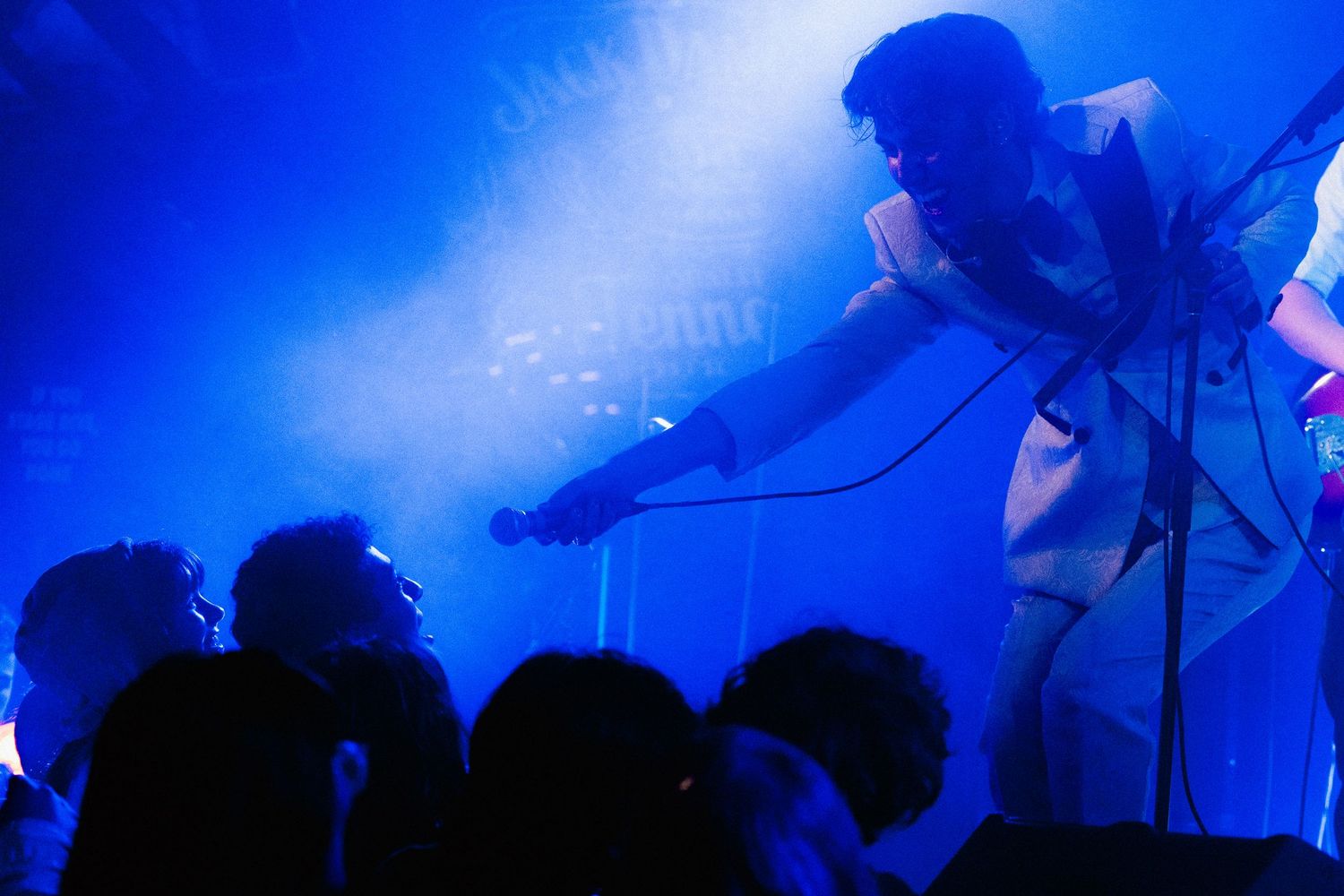 Performer leaning toward crowd on stage under dramatic blue concert lighting.