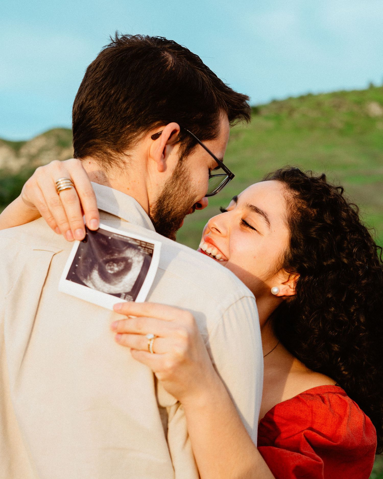 Happy couple smiling and holding ultrasound photo together outdoors for pregnancy announcement.
