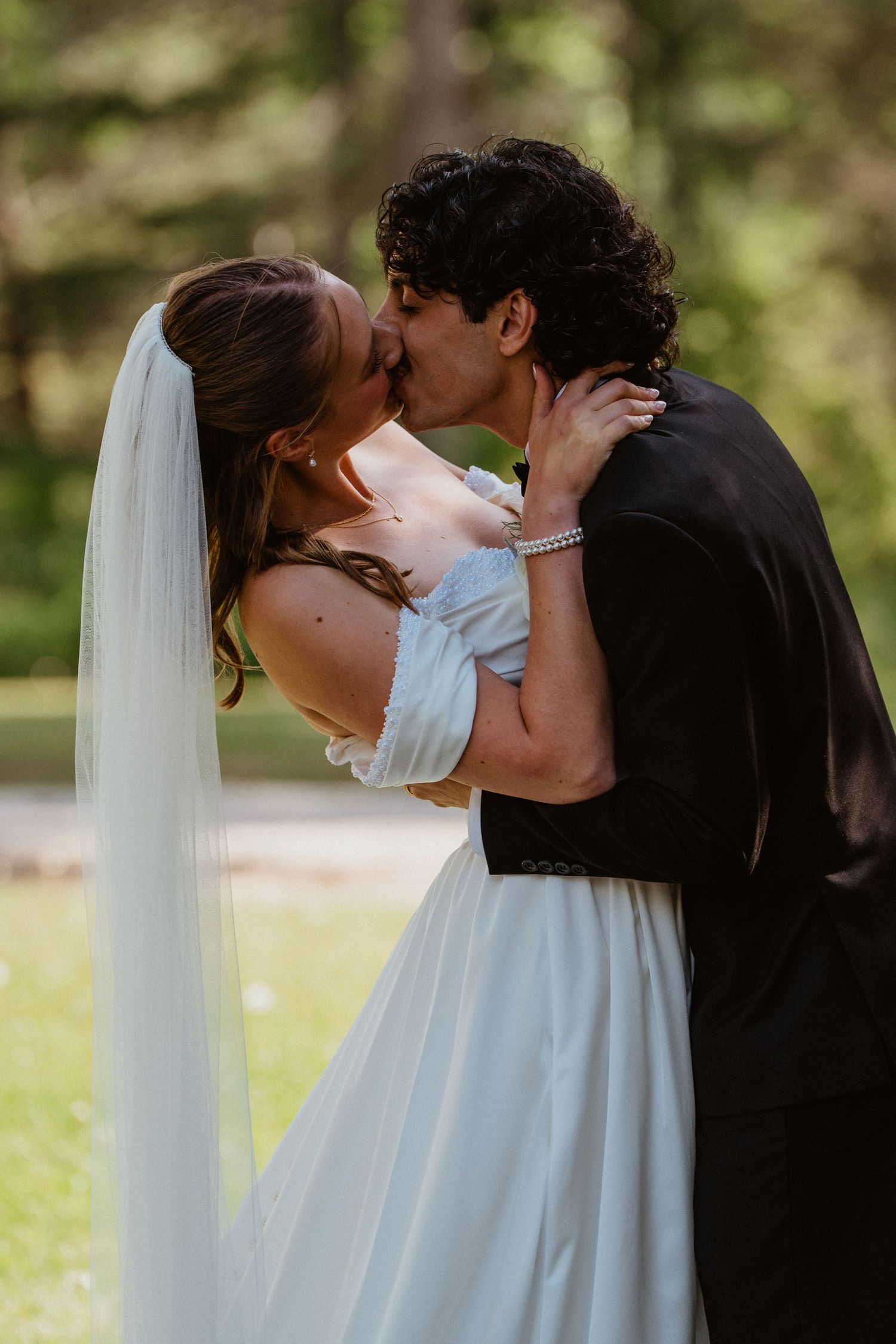 A bride and groom share their first kiss as newlyweds outdoors, with the brides veil flowing gracefully.