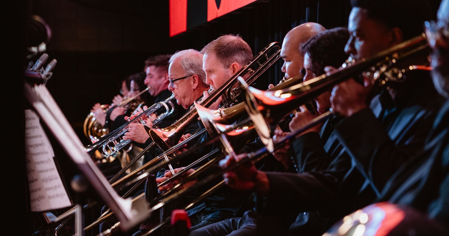 Row of brass musicians playing trumpets and trombones in orchestra.
