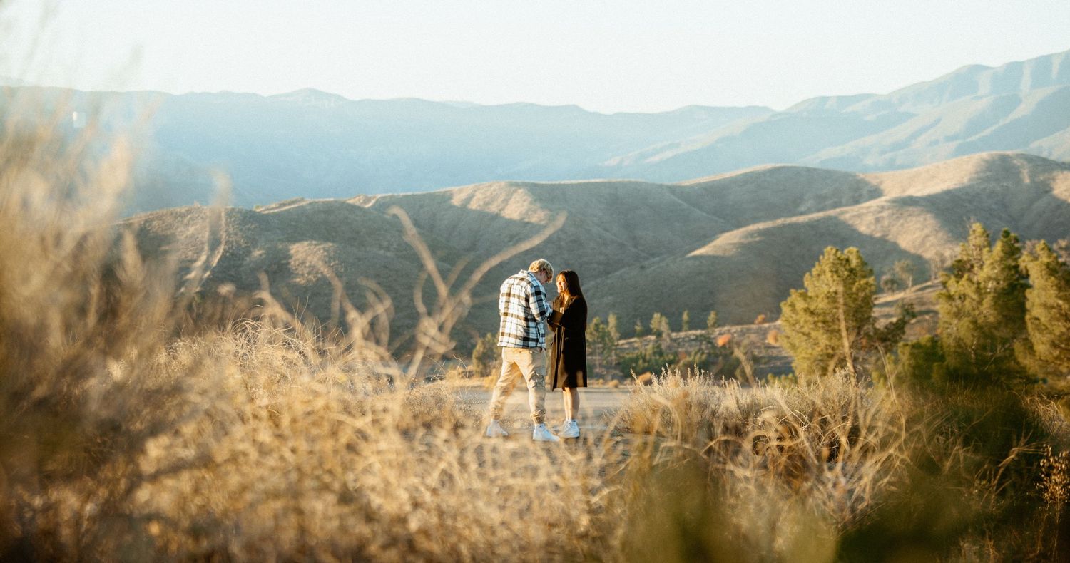 Couple standing together overlooking a stunning mountain landscape at golden hour.