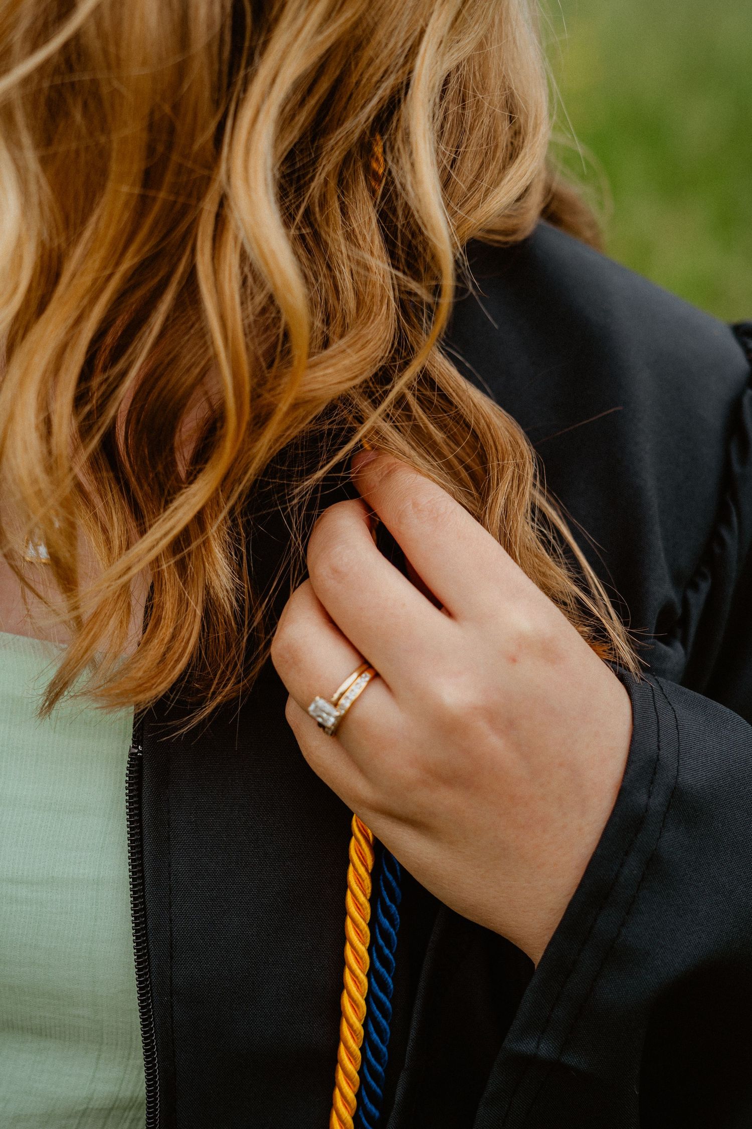 Close-up of a graduate holding her black gown with a diamond ring and gold honor cord visible.