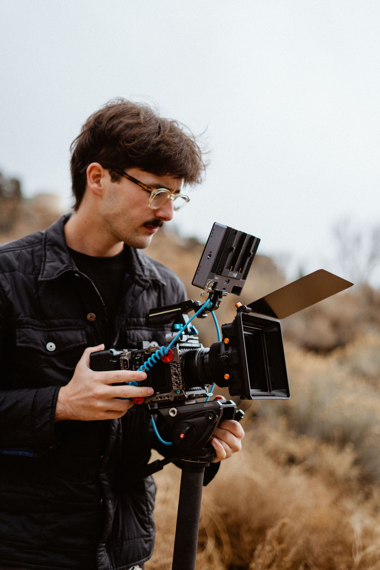 Young male videographer holding a professional cinema camera rig outdoors in nature.