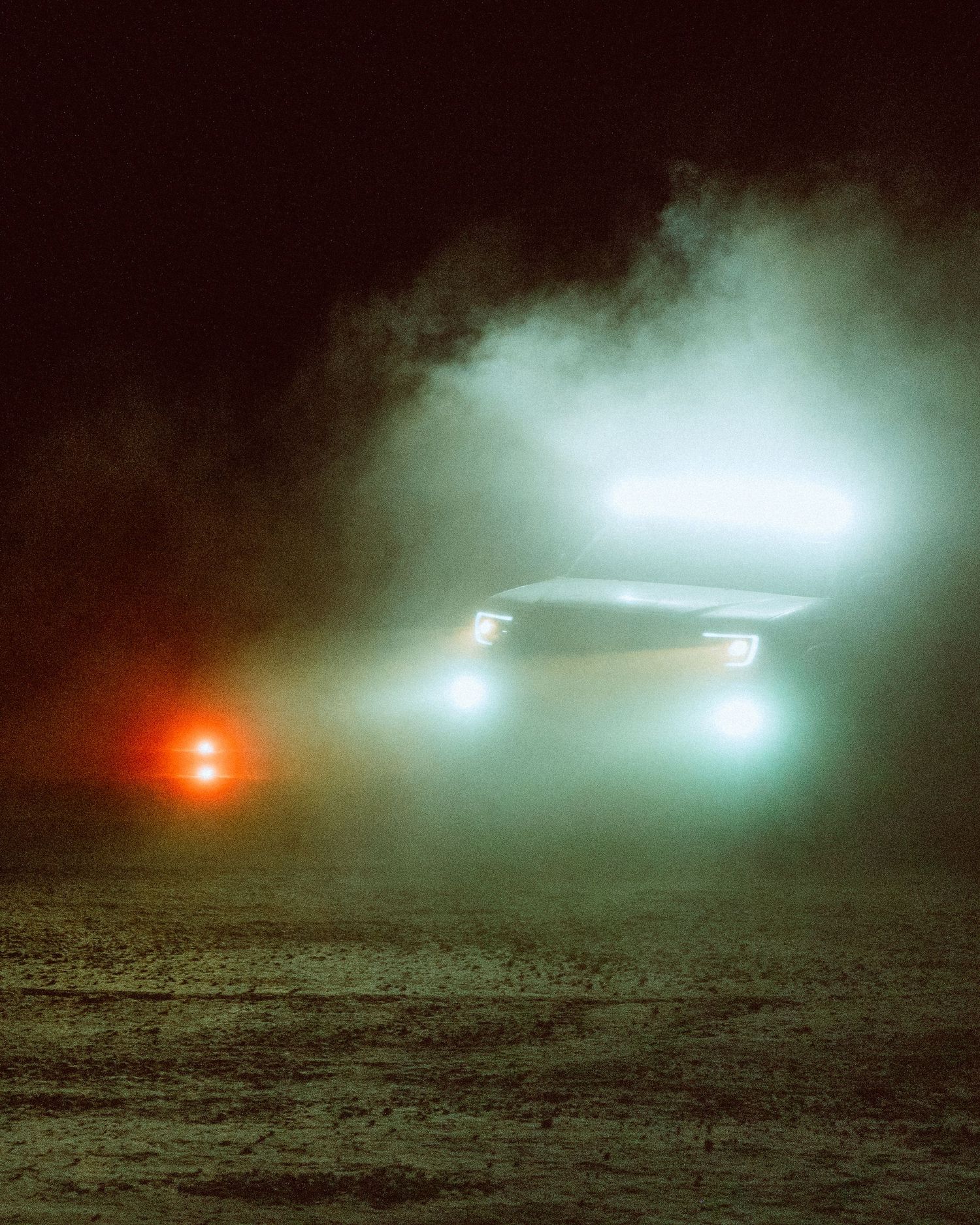 Two vehicles with bright headlights cutting through thick fog or dust on a dark night.