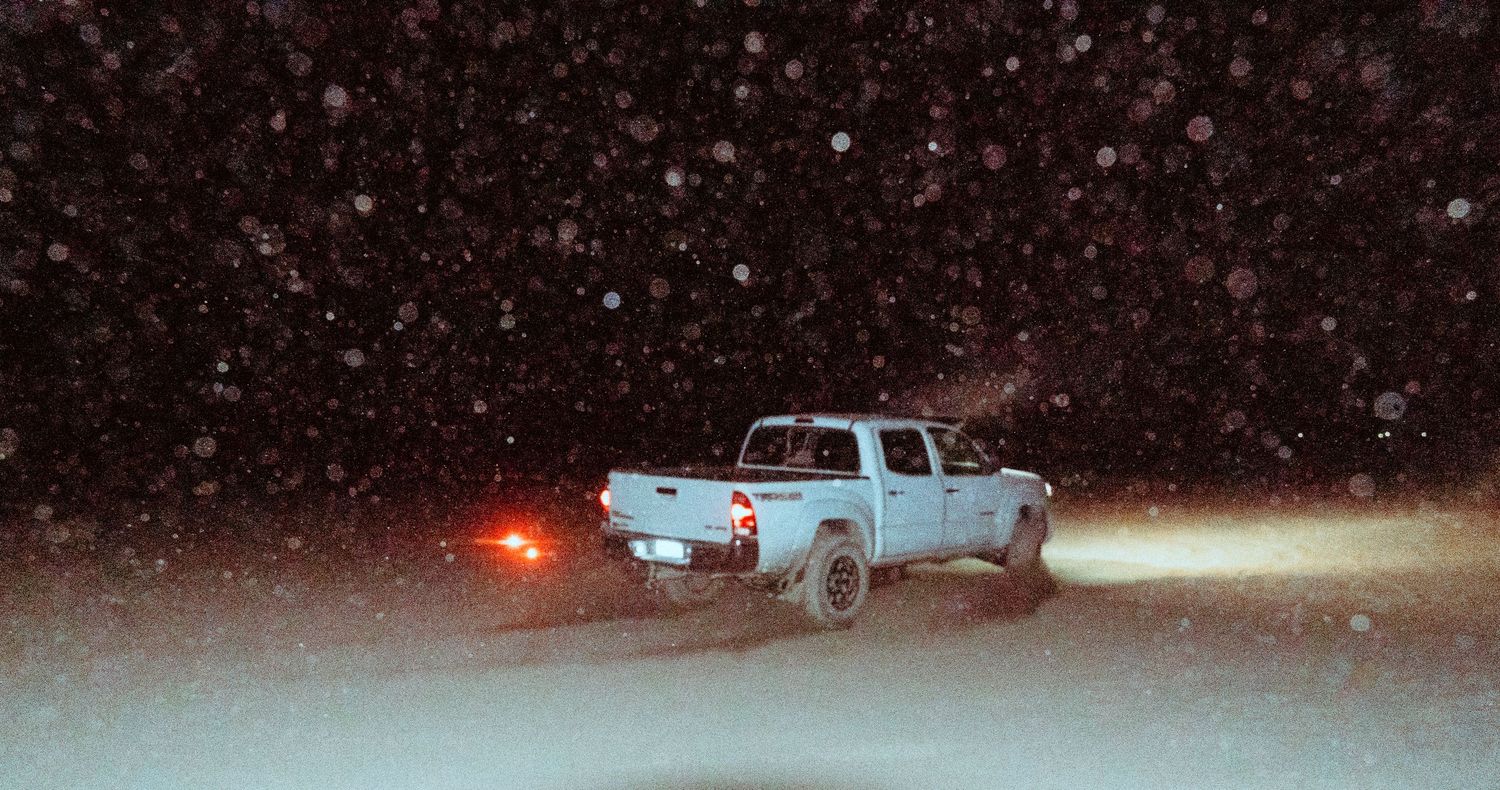 Pickup truck driving through a heavy snowstorm at night on an open snowy field.