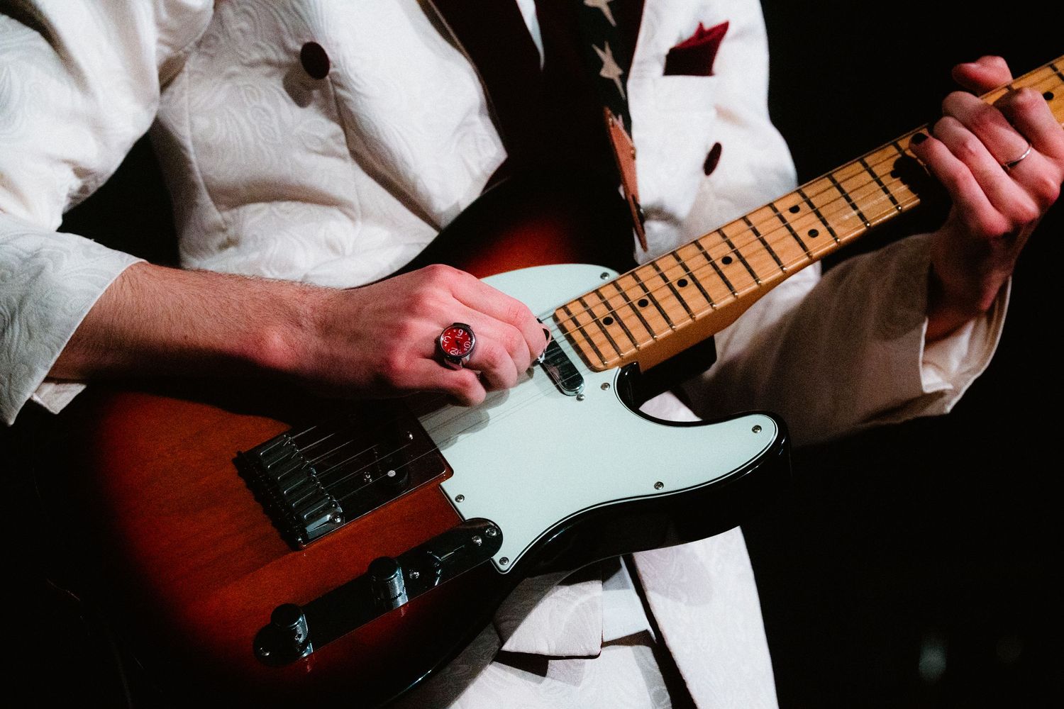 Musician in white suit playing a sunburst Fender Telecaster electric guitar on stage.