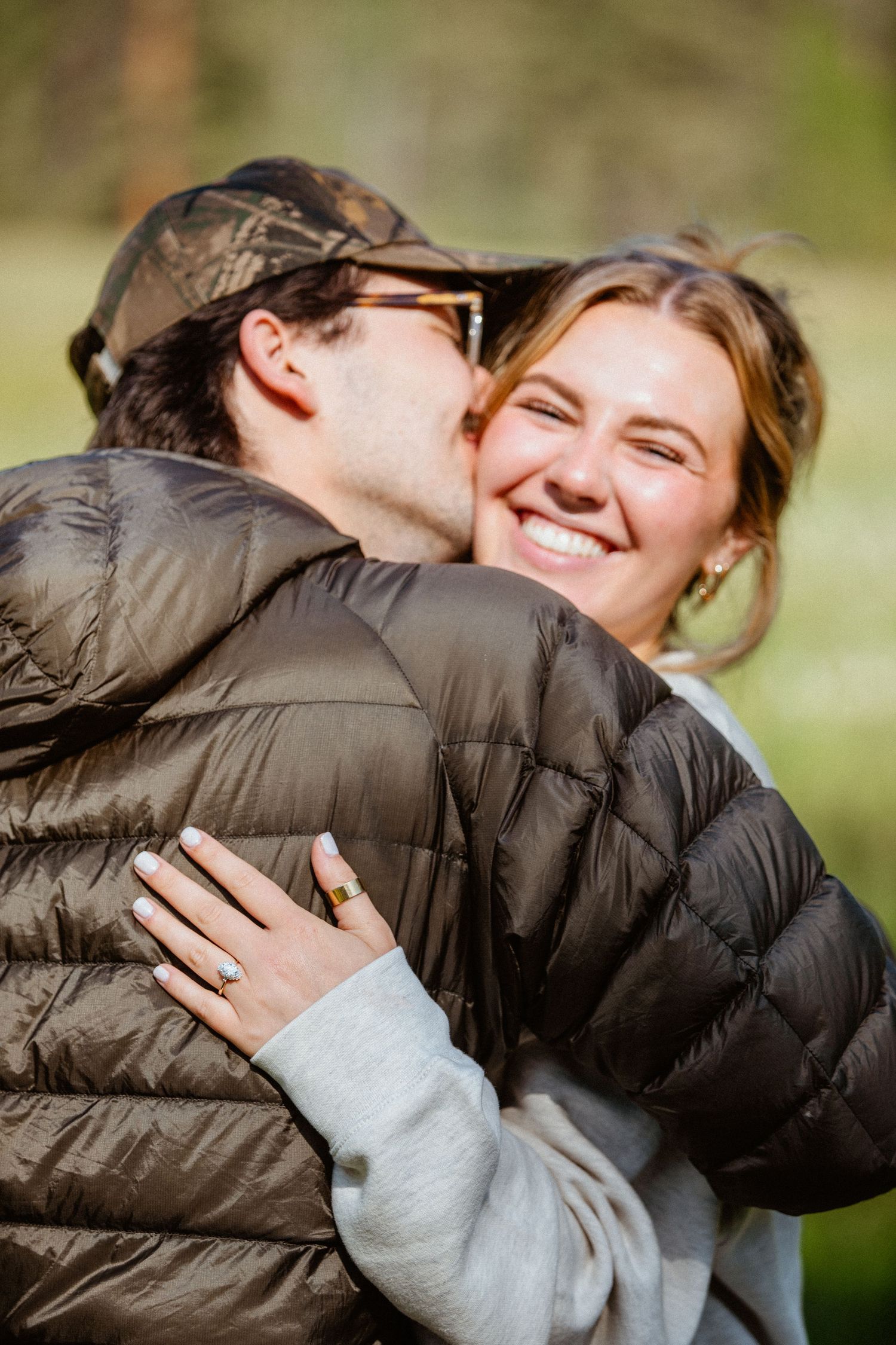 Newly engaged couple embracing, woman smiling with engagement ring visible on her hand.