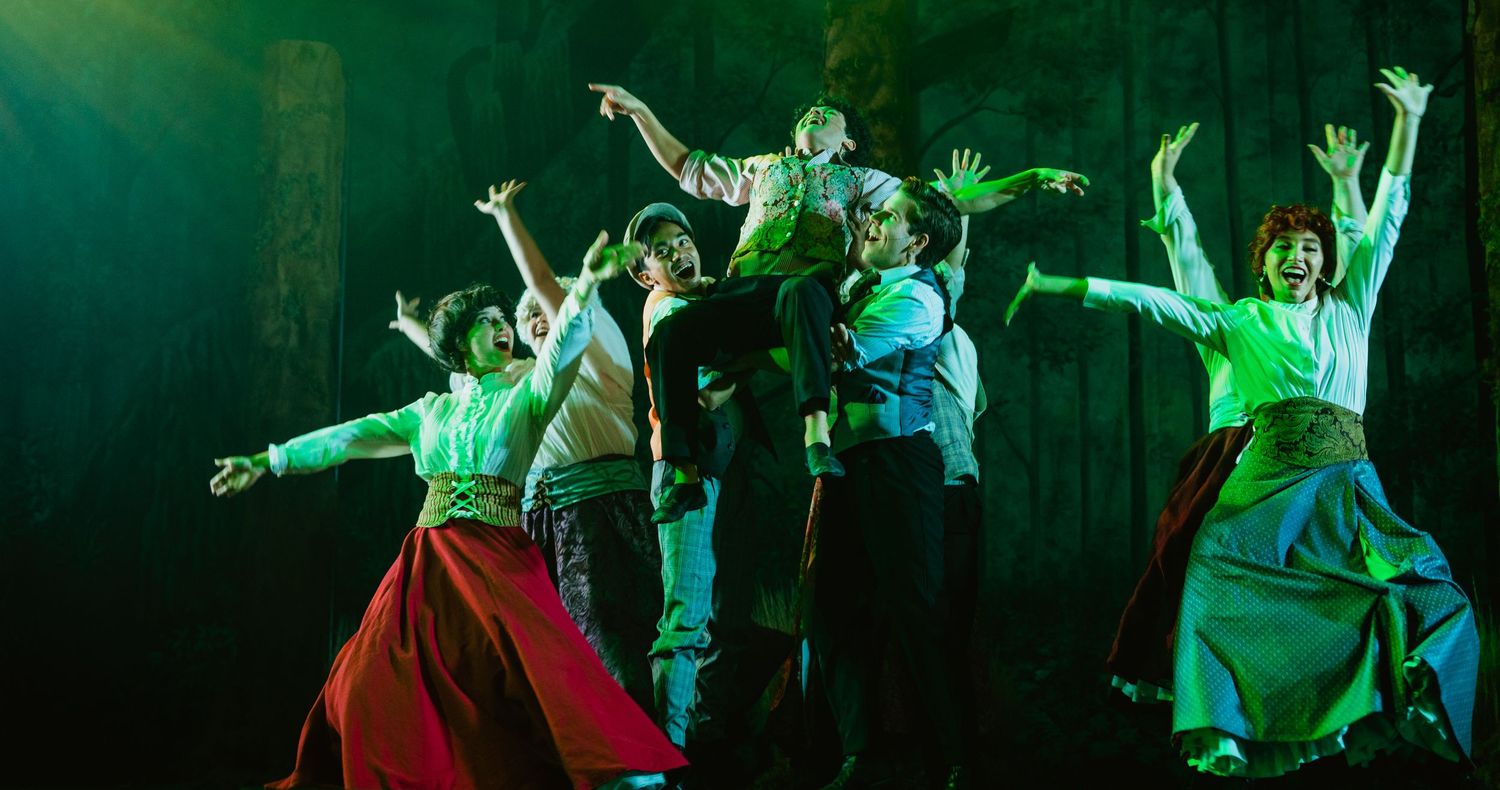 A dynamic group of dancers strikes dramatic poses under green stage lighting during a performance.