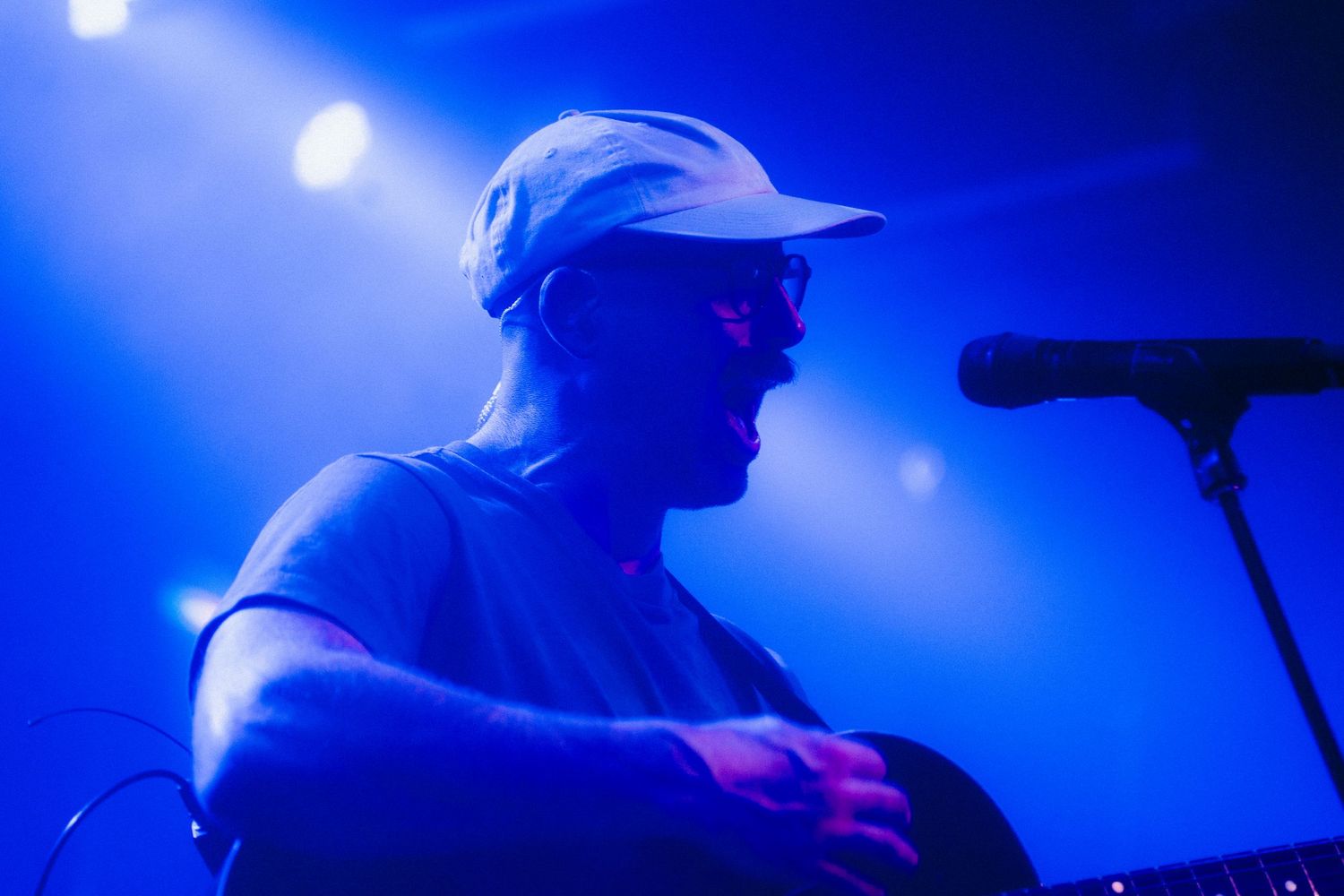 Close-up profile of a musician wearing a white cap performing under blue stage lighting.
