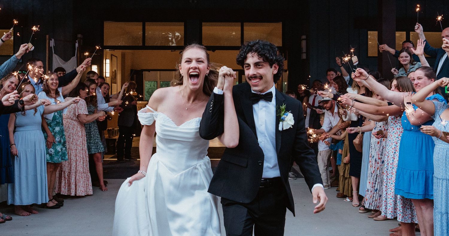 Joyful bride and groom exit wedding ceremony through sparkler tunnel surrounded by cheering guests.