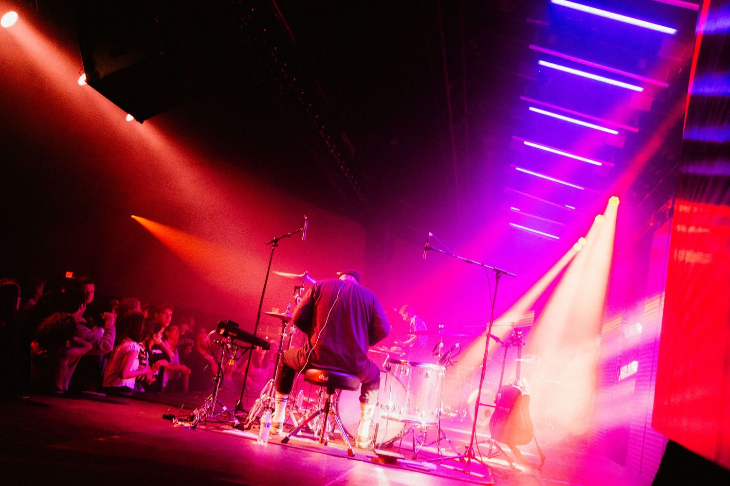 Band performing on a colorful stage with purple and orange lighting at a live concert.