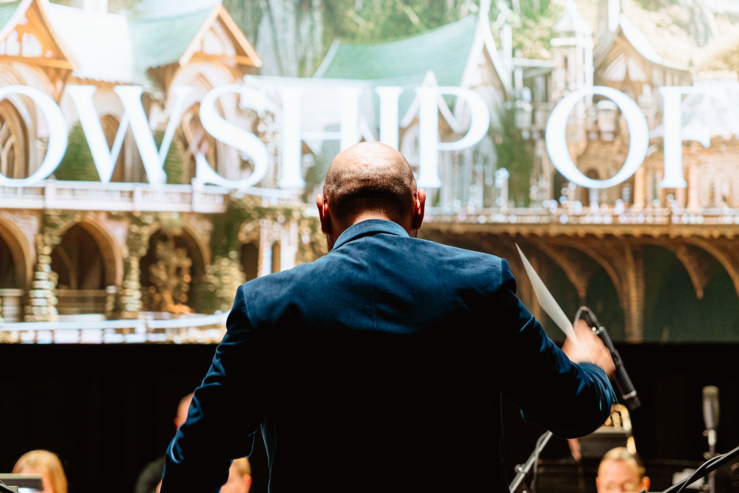 Orchestra conductor seen from behind leading Fellowship of the Ring live film score performance.