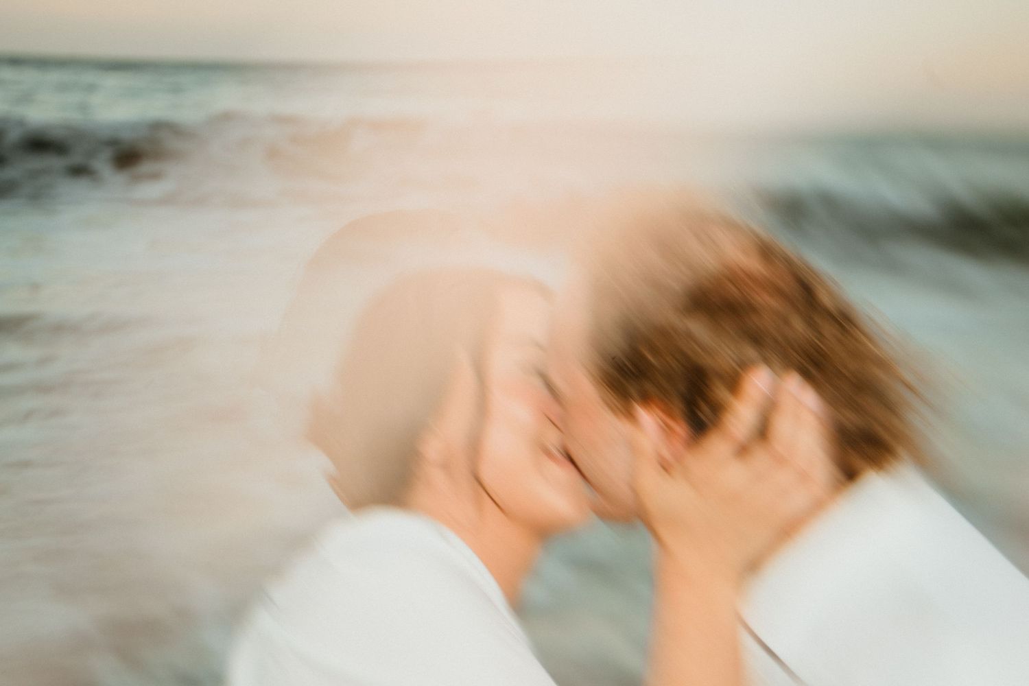 Couple sharing a romantic kiss on the beach with golden sunset light.