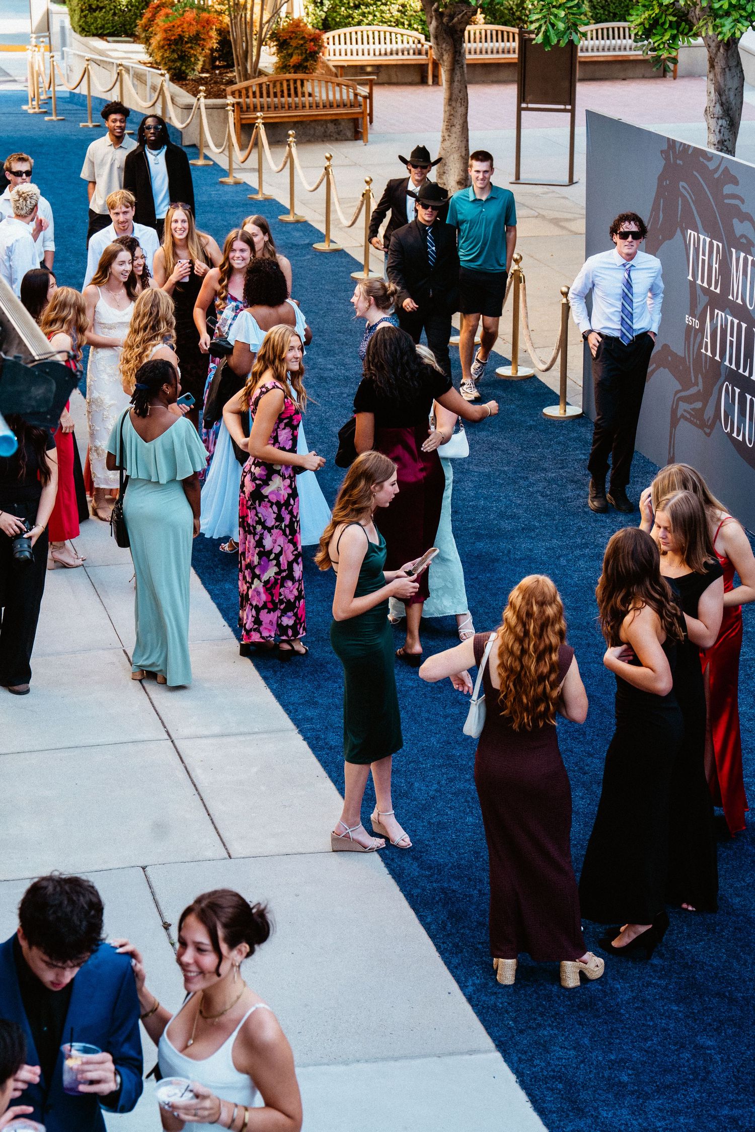 Elegantly dressed guests walking on a blue carpet at a formal event outside a venue.