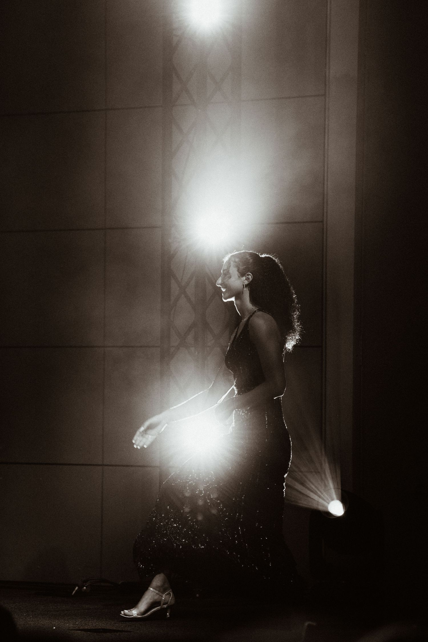 Elegant woman walks in dramatic spotlight with lens flare in stunning black and white stage photography.