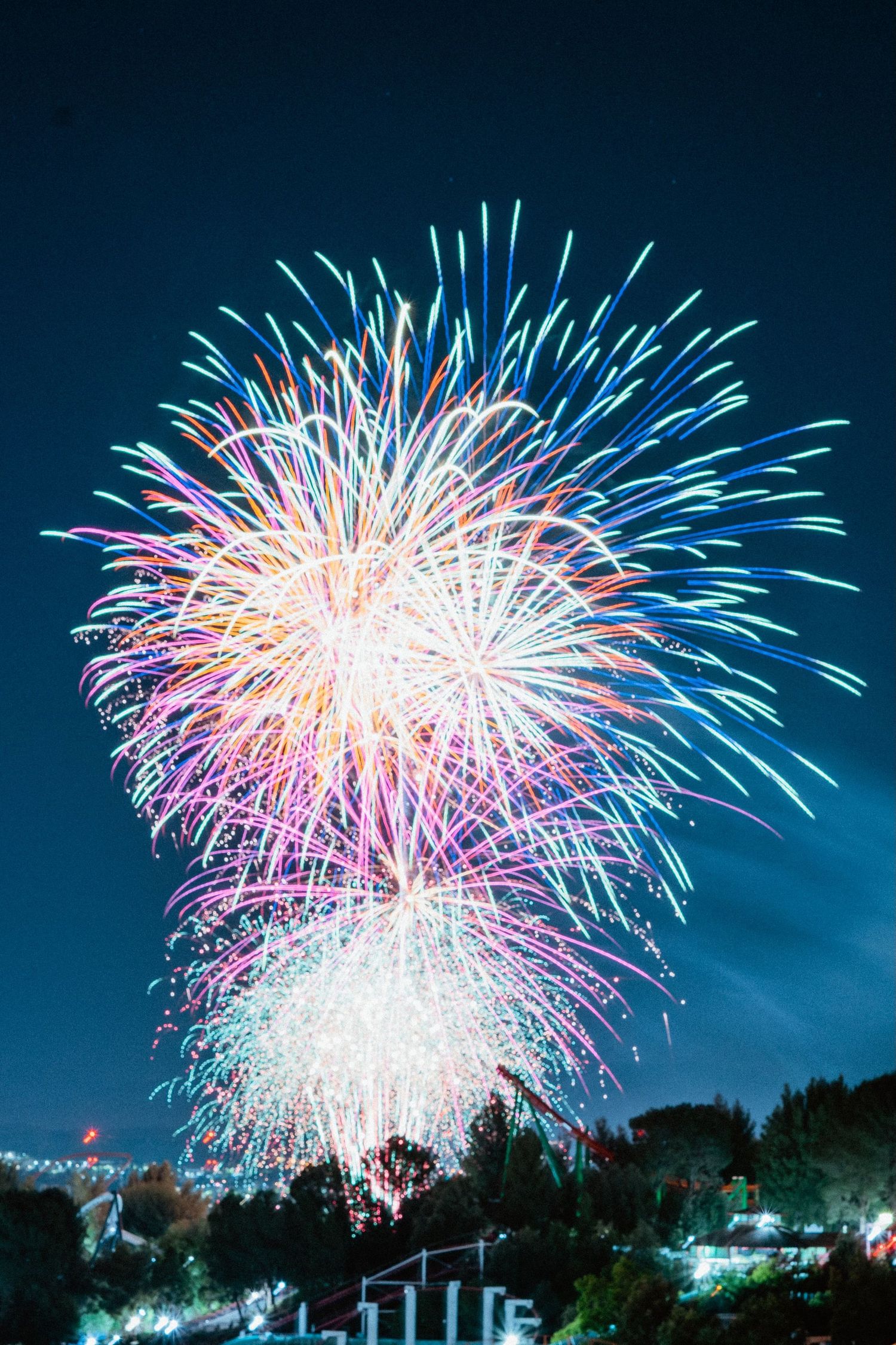 Colorful fireworks exploding in night sky over city with pink blue and white bursts.