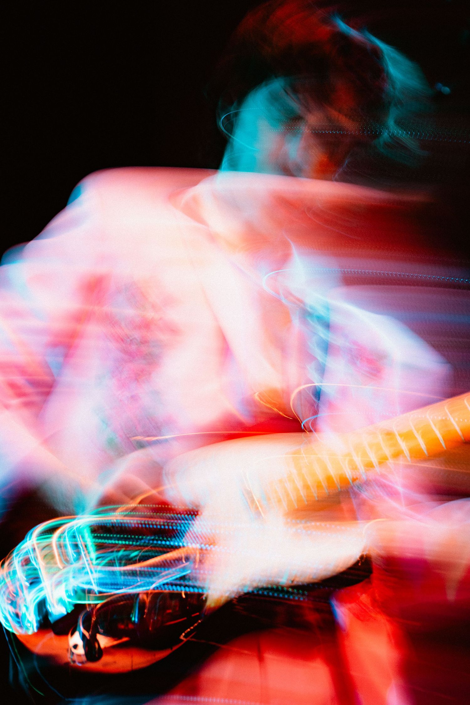 Abstract motion blur photo of electric guitar player performing with colorful red and blue lights.