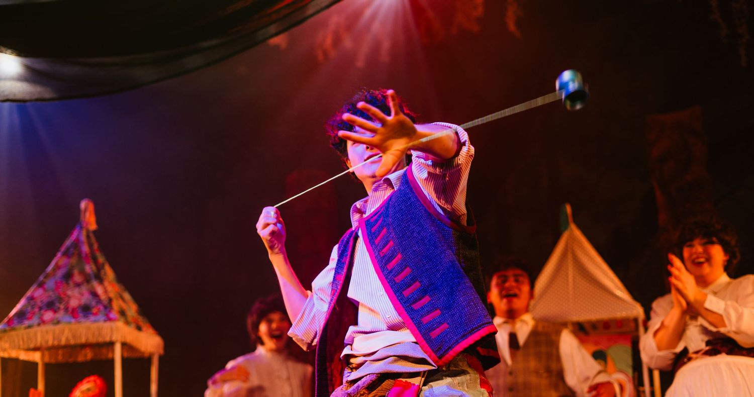 A performer in traditional costume spins a prop on stage during a vibrant cultural performance.