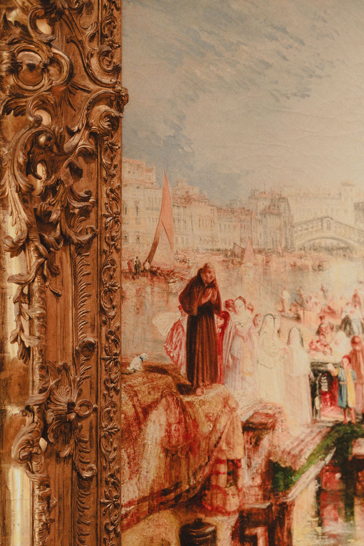 Close-up of an ornate gilded picture frame beside a classical oil painting depicting a Venetian scene.