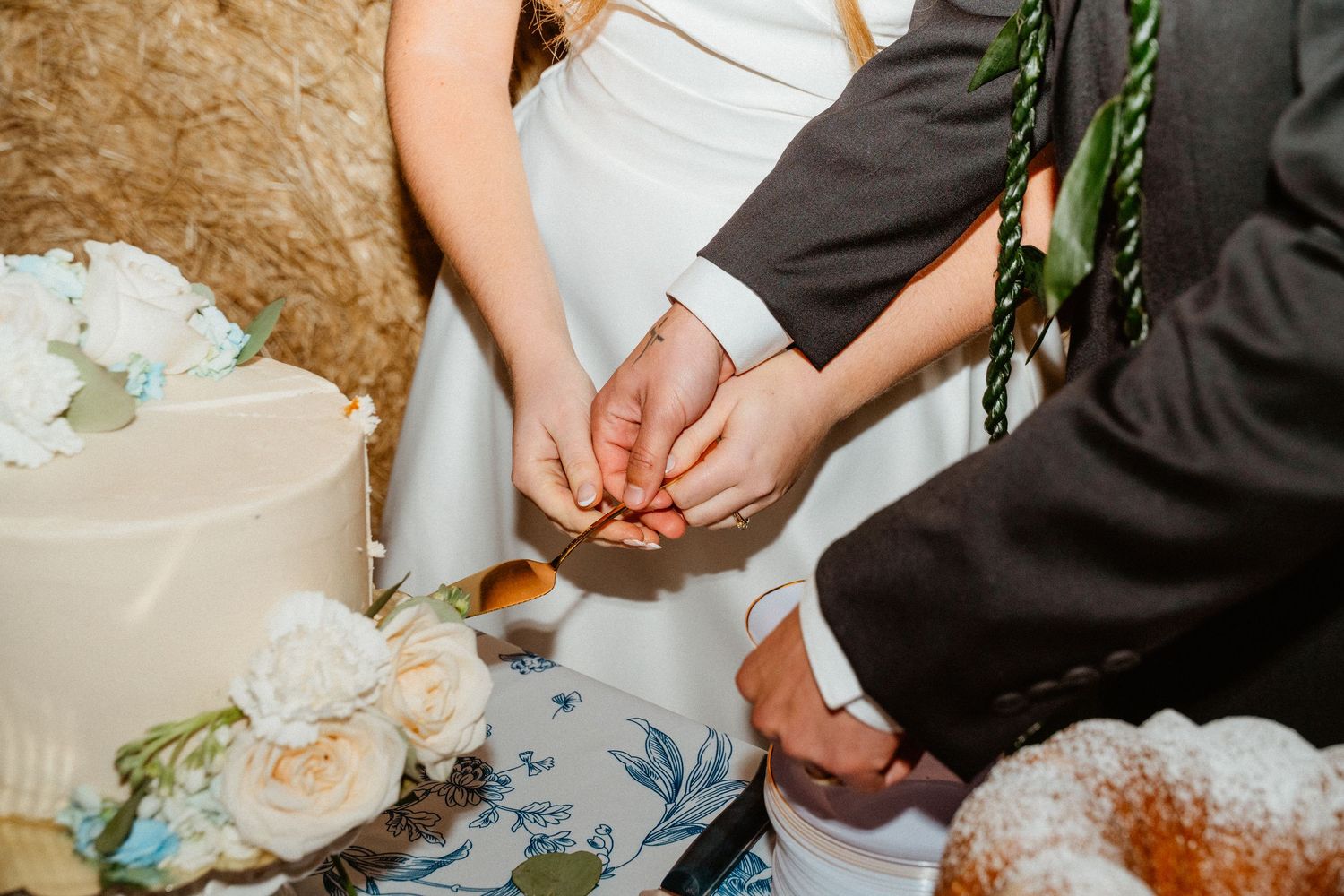 Bride and groom cutting wedding cake together at rustic barn reception with white floral decorations.