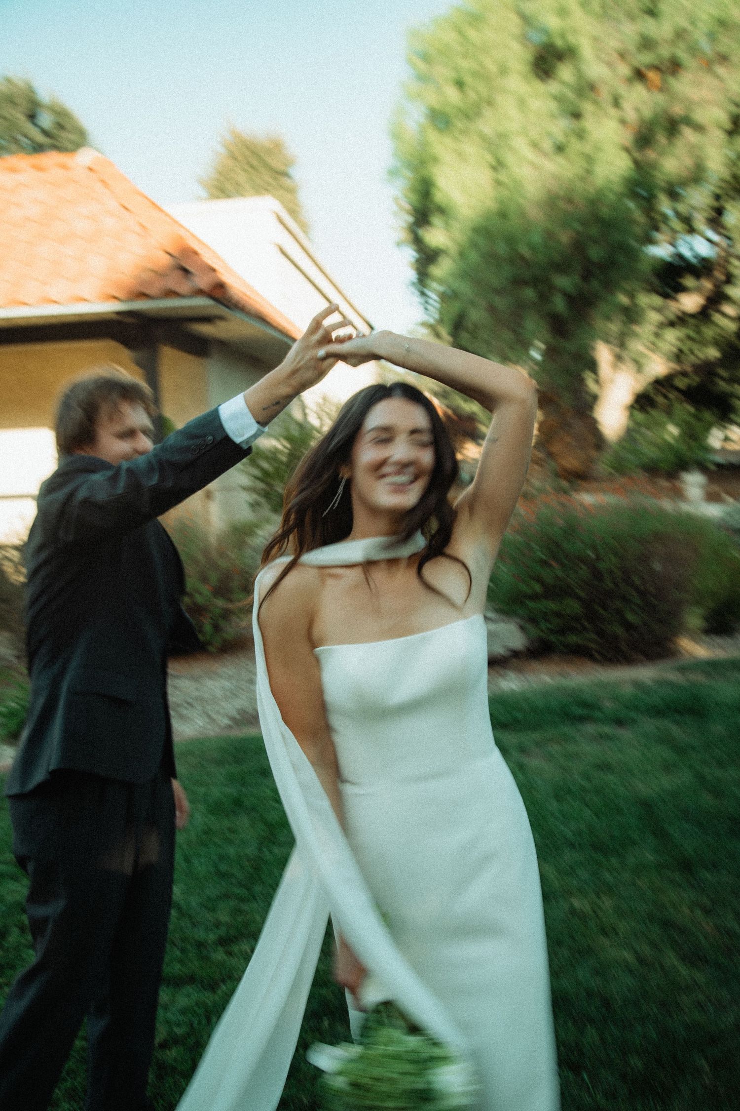 Bride in elegant white gown twirling joyfully with groom in garden setting.