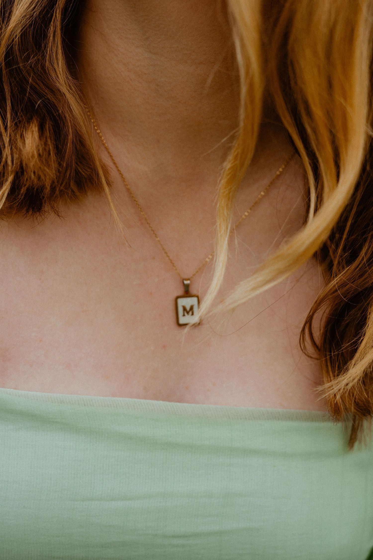 Close-up of gold initial M pendant necklace on woman in mint green top.