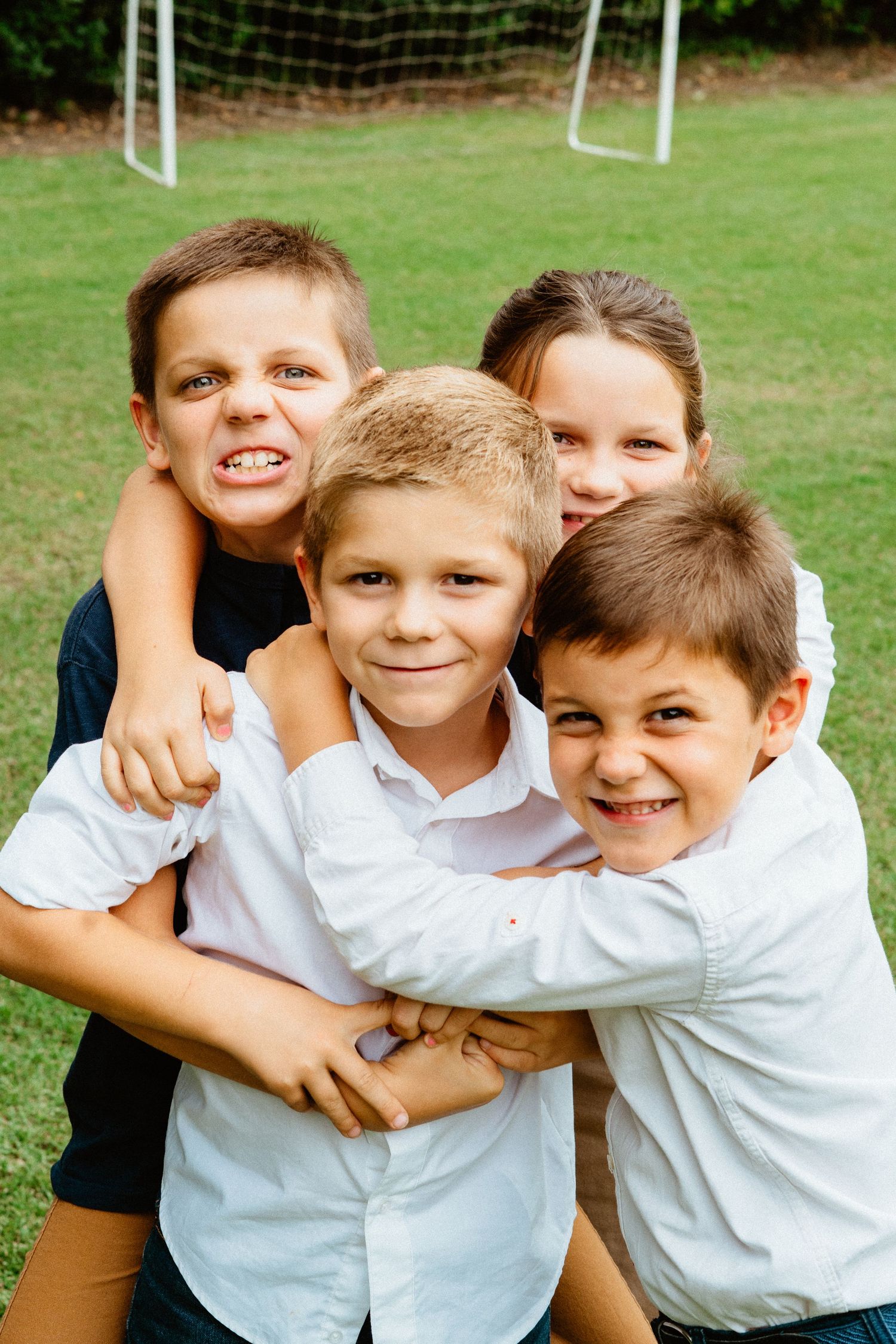 Four siblings hugging and smiling together on a green grassy field.