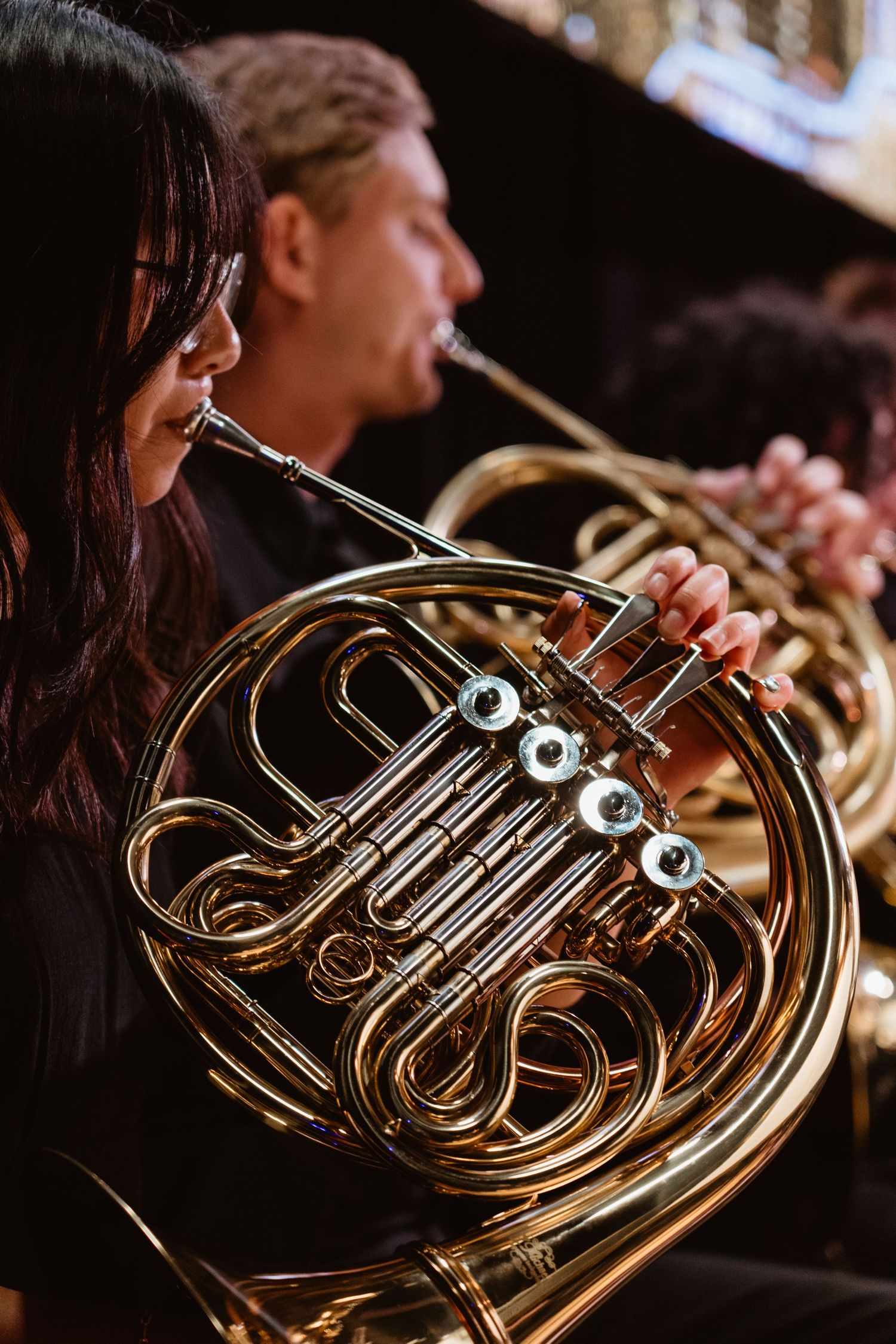 Musicians playing French horns in an orchestra performance on stage.