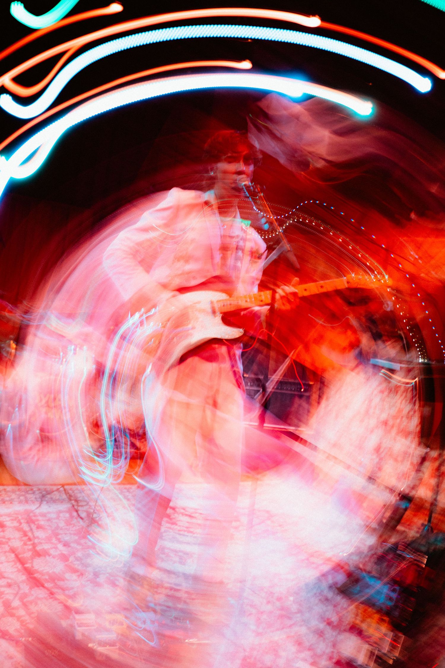 Swirling abstract long exposure shot of wedding guitarist performing under colorful neon red and blue stage lights.