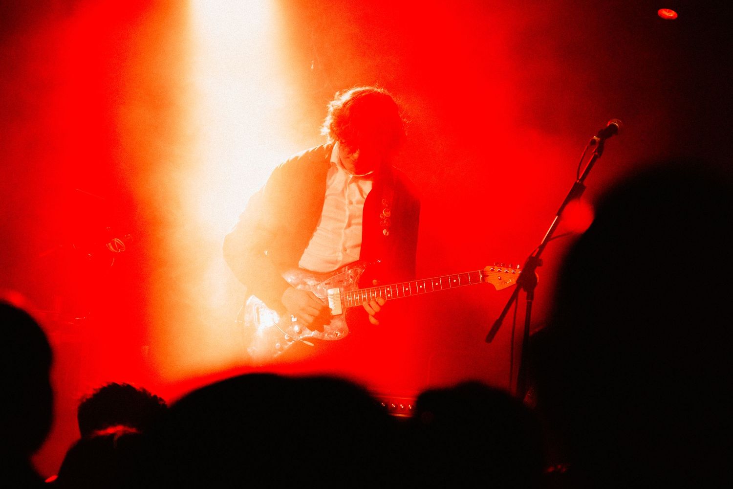A musician plays an electric guitar against a hazy red and orange background.