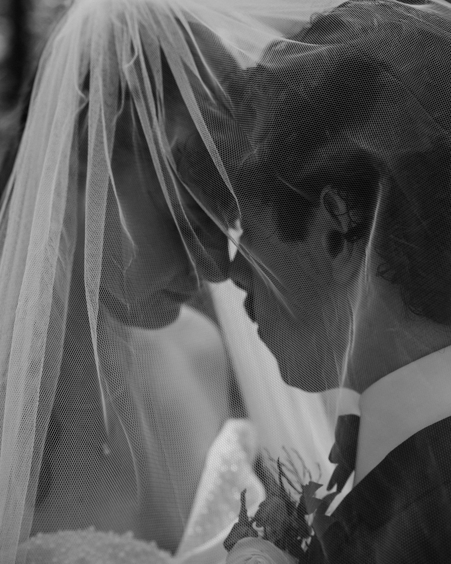 Romantic black and white photo of bride and groom sharing an intimate moment under a flowing veil.