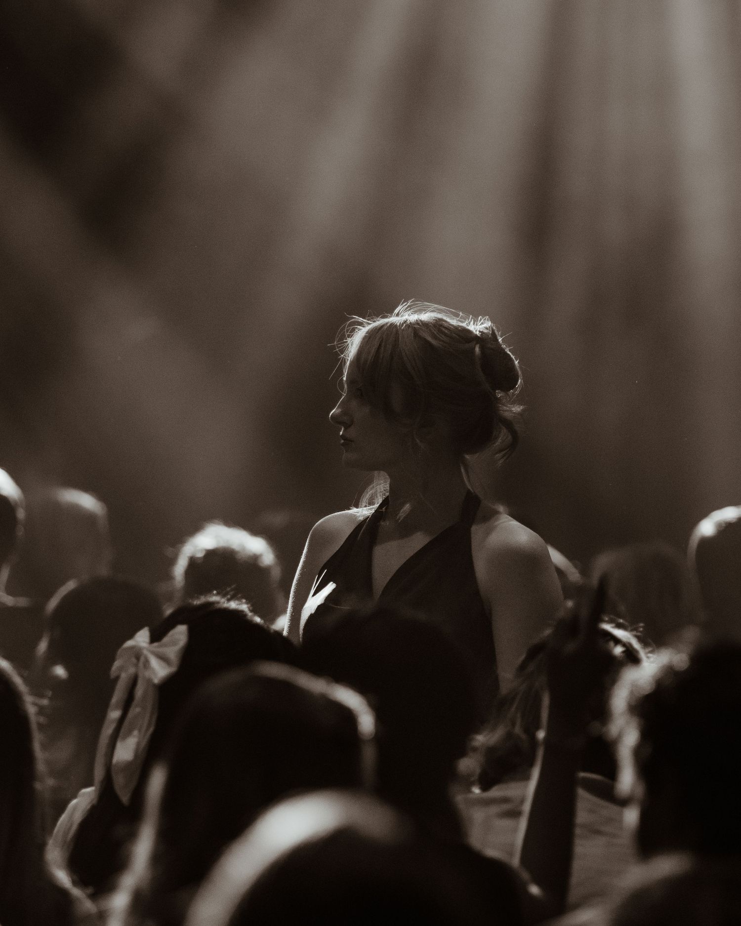 Elegant woman standing in spotlight among seated concert audience.