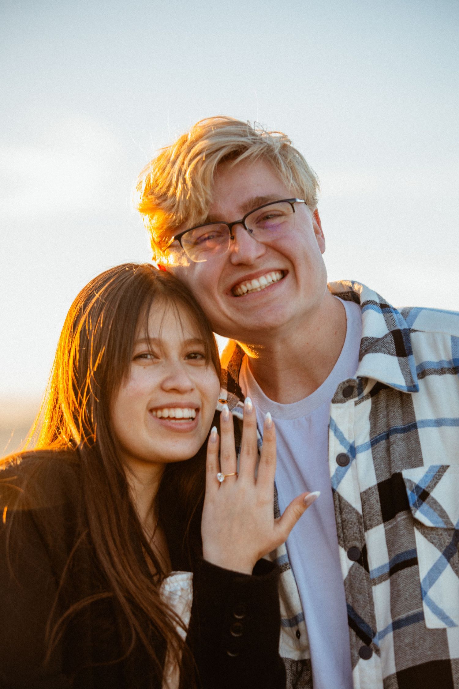 Happy engaged couple smiling at sunset with woman showing off her engagement ring.