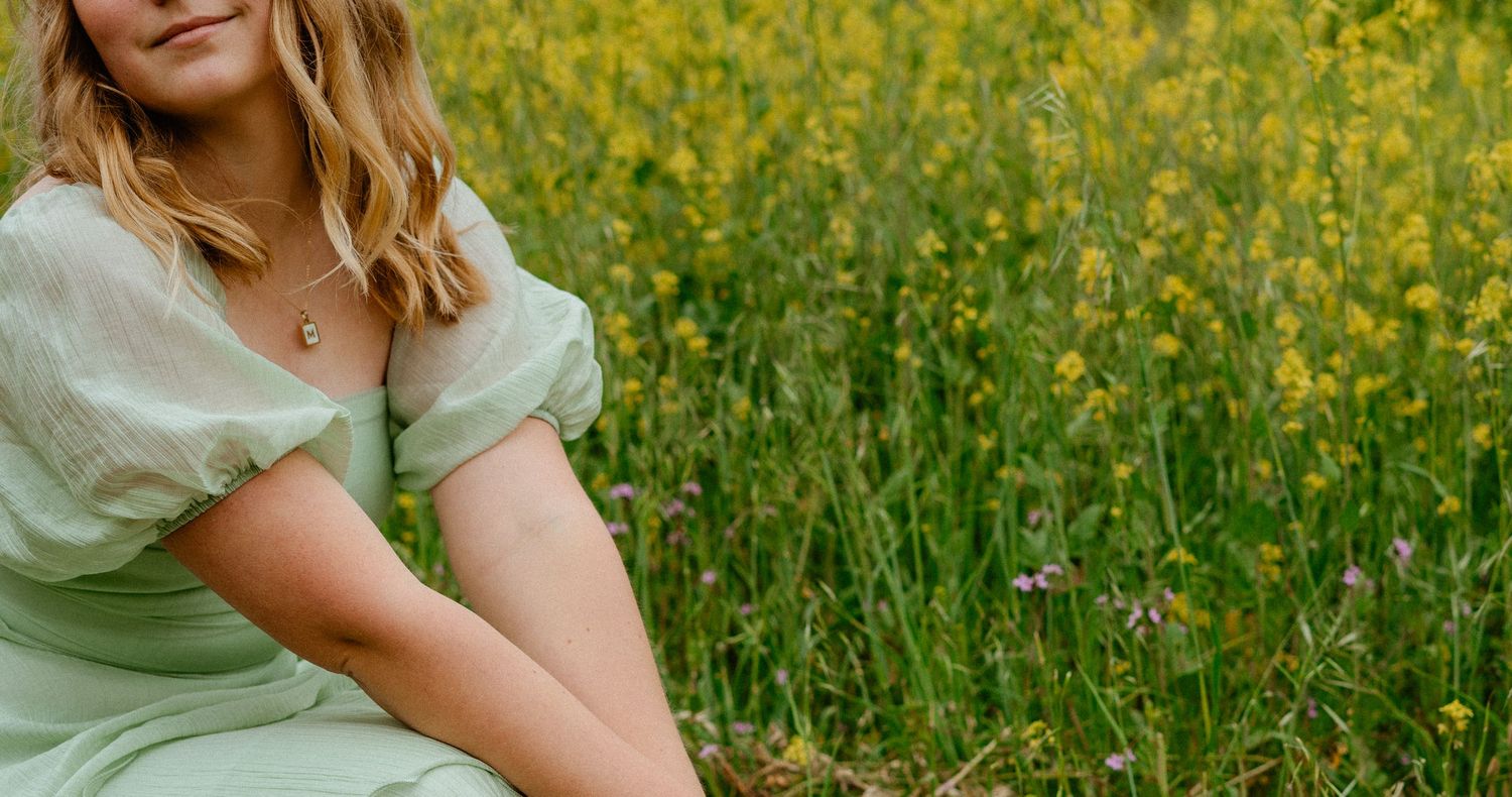 Young woman in mint green dress sitting in field of yellow wildflowers.