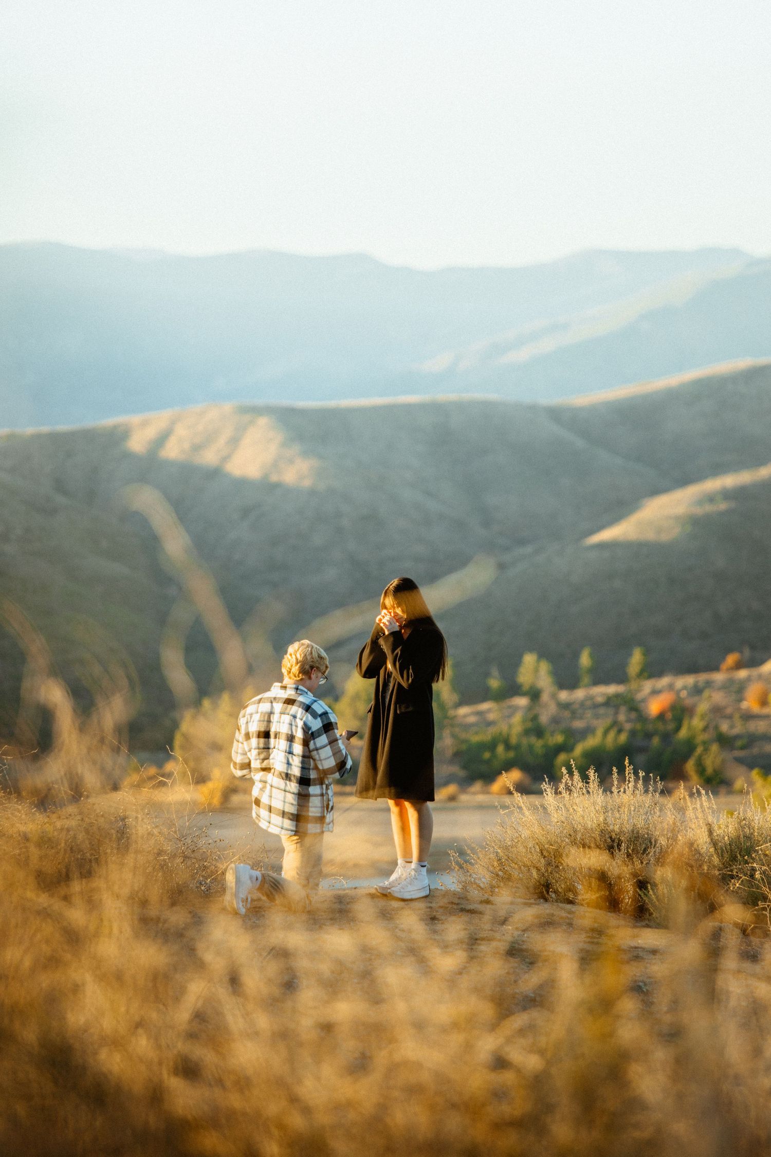 Man kneeling to propose to woman at sunset with breathtaking mountain views behind them.
