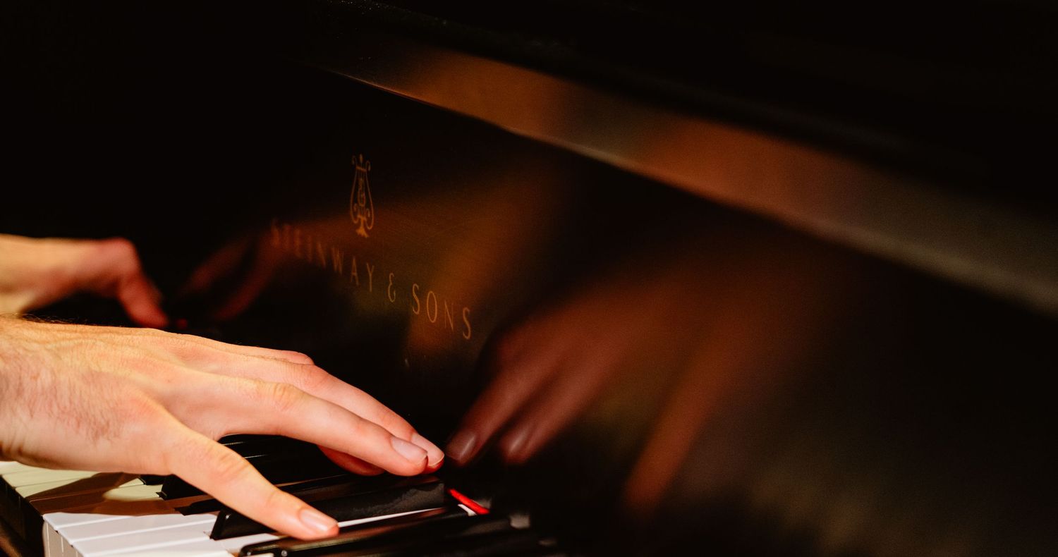 Close-up of hands playing a grand piano in dramatic low lighting.