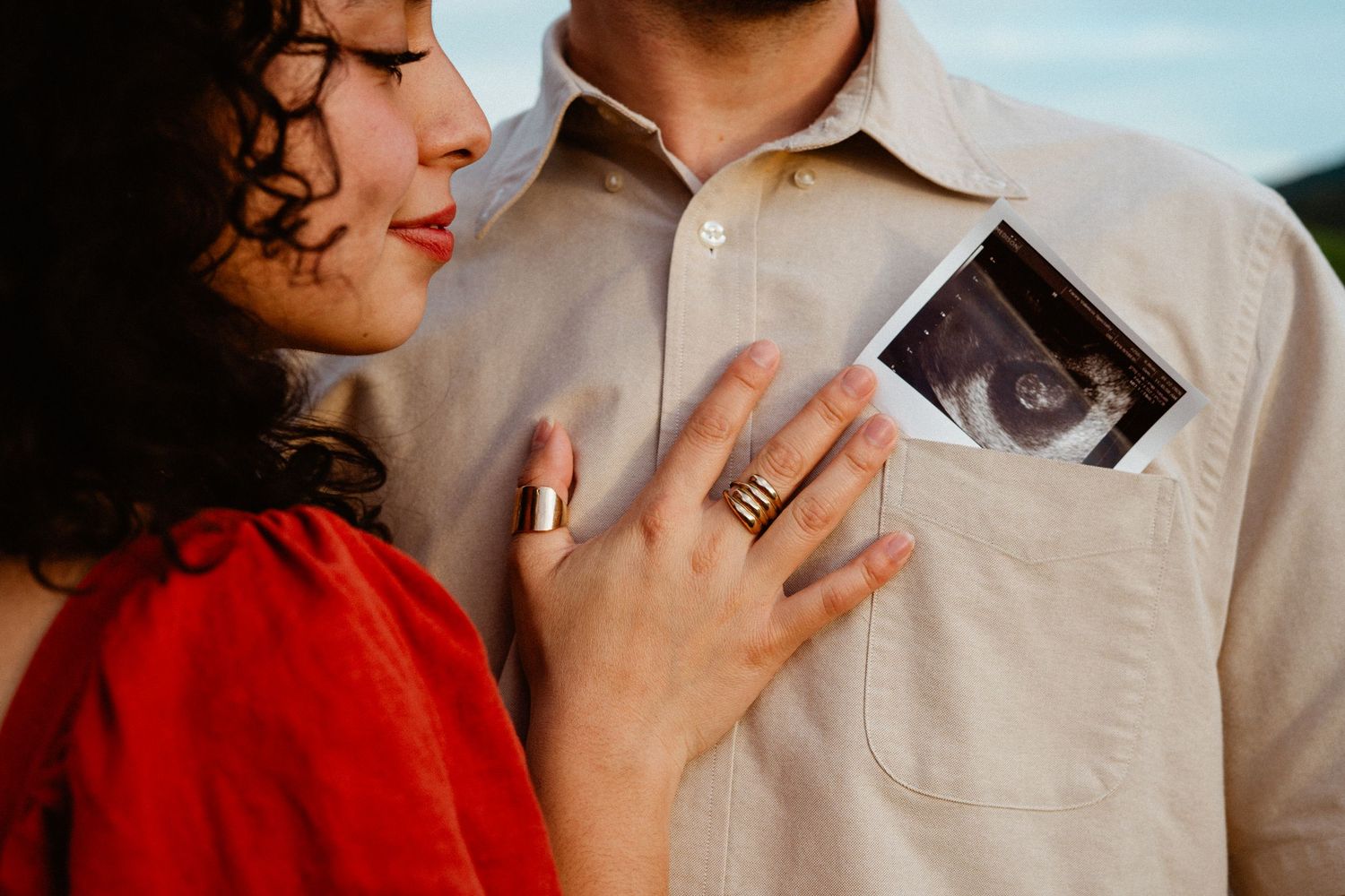 Couple sharing tender moment, woman in red touching man's chest with ultrasound photo in pocket.