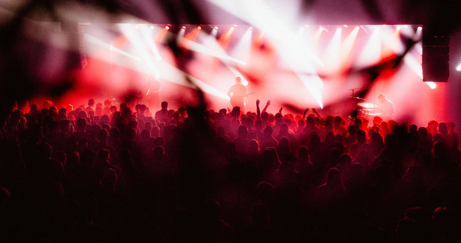 Silhouette of concert crowd under vibrant red stage lighting at a live music event.