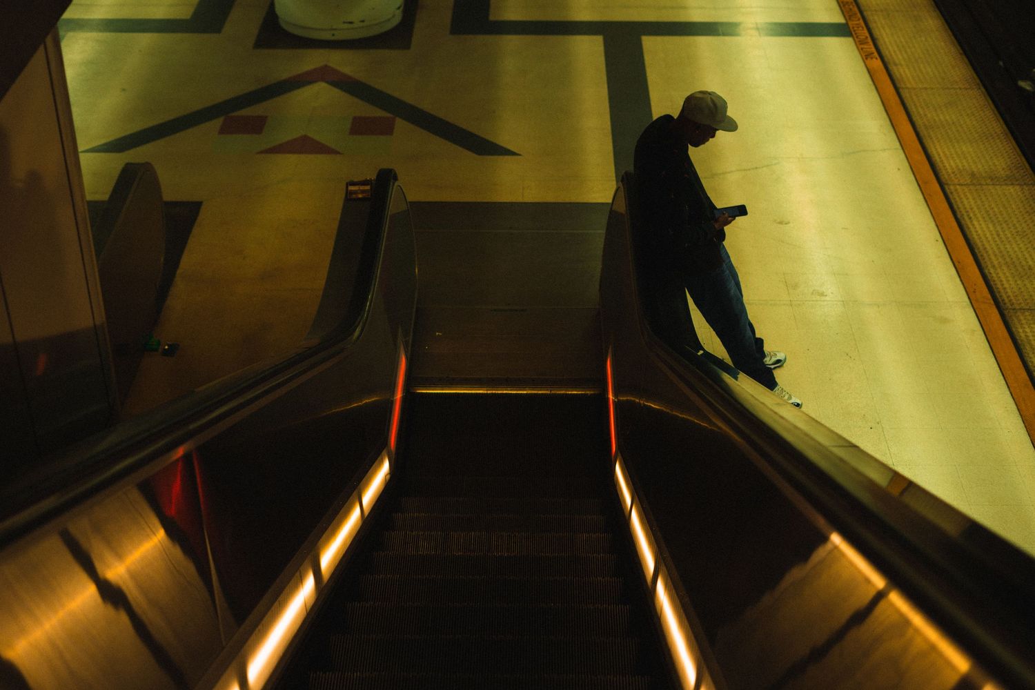 A man on an escalator in a dimly lit subway station checks his phone.