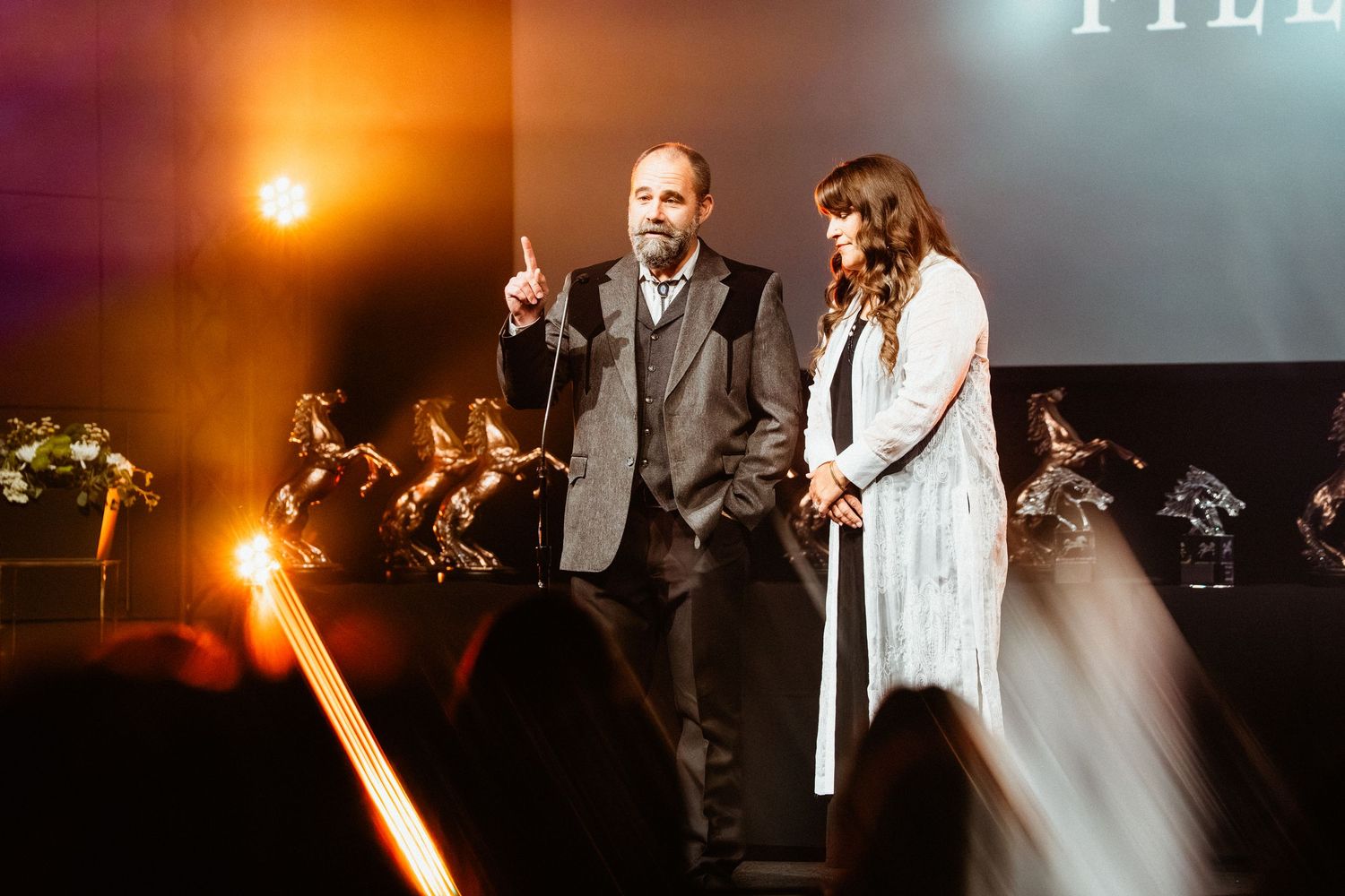 Two elegantly dressed presenters on a dimly lit stage during an awards ceremony event.