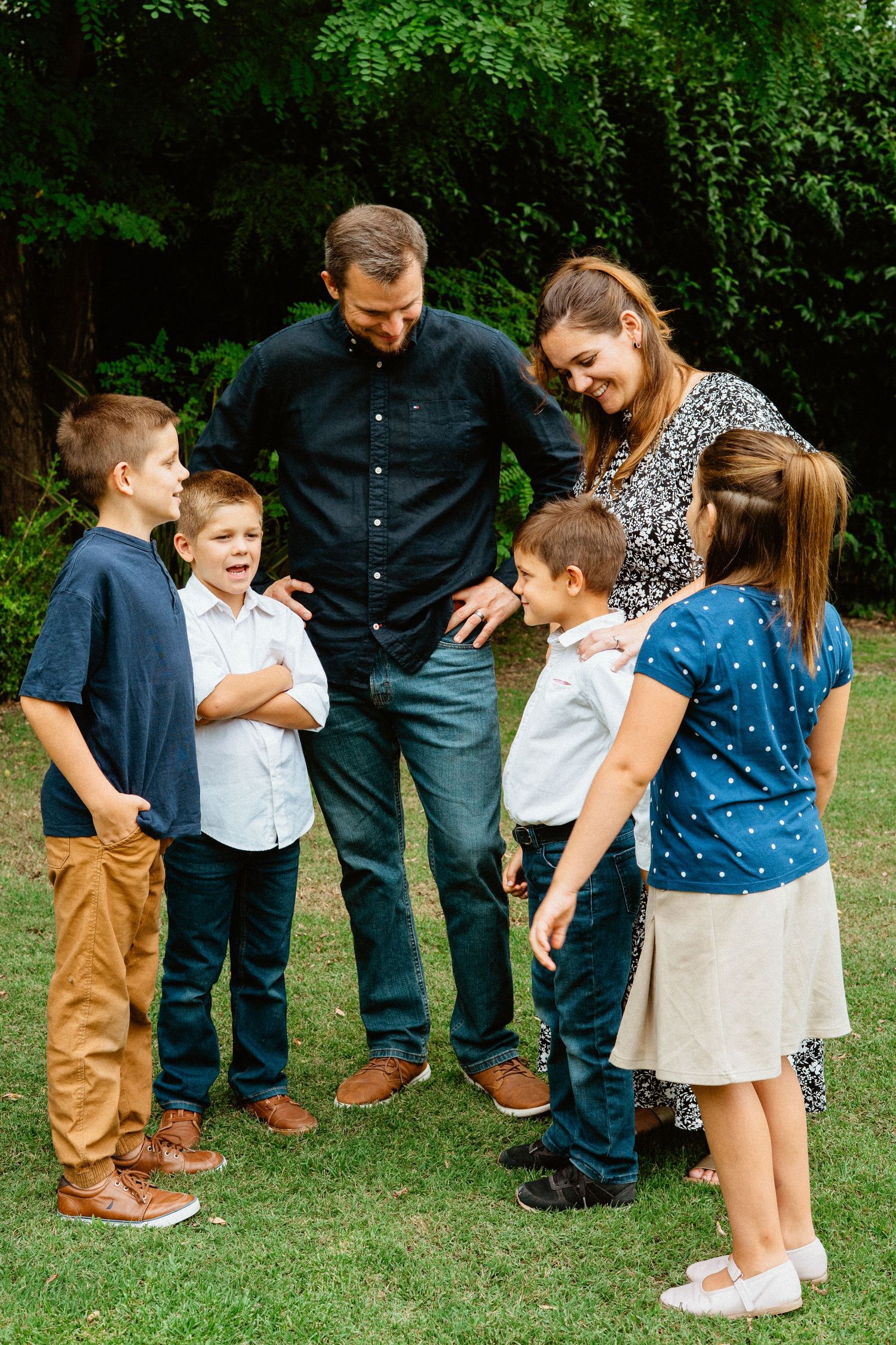 Parents and four children gathered together laughing in a green yard.
