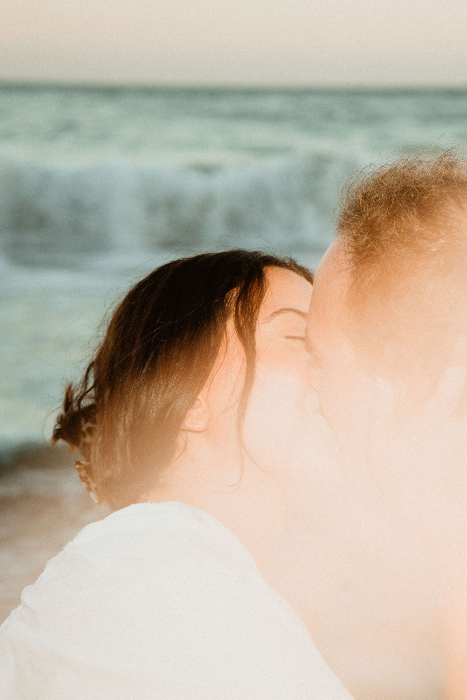 Romantic couple sharing a tender moment at sunset on the beach with ocean waves in background.