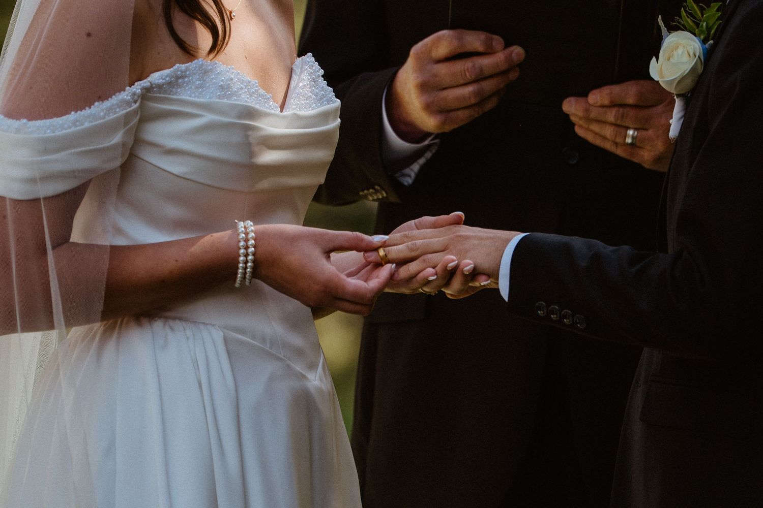 Bride and groom exchanging rings during wedding ceremony, officiant holding book in background.